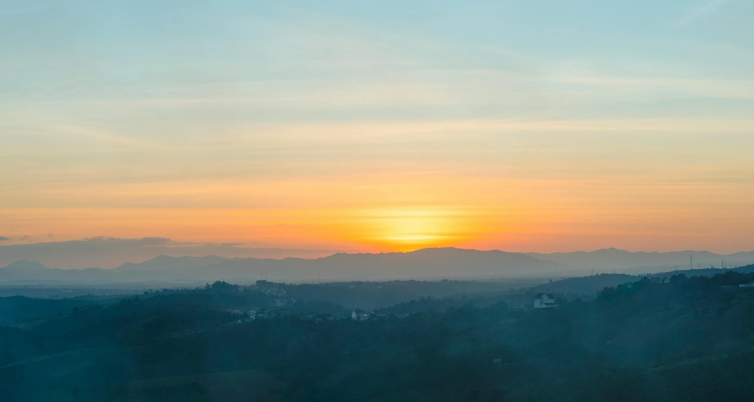 A scenic view of a sunset over mountains, with the sky painted in soft pastel colors and a layered landscape in the foreground.