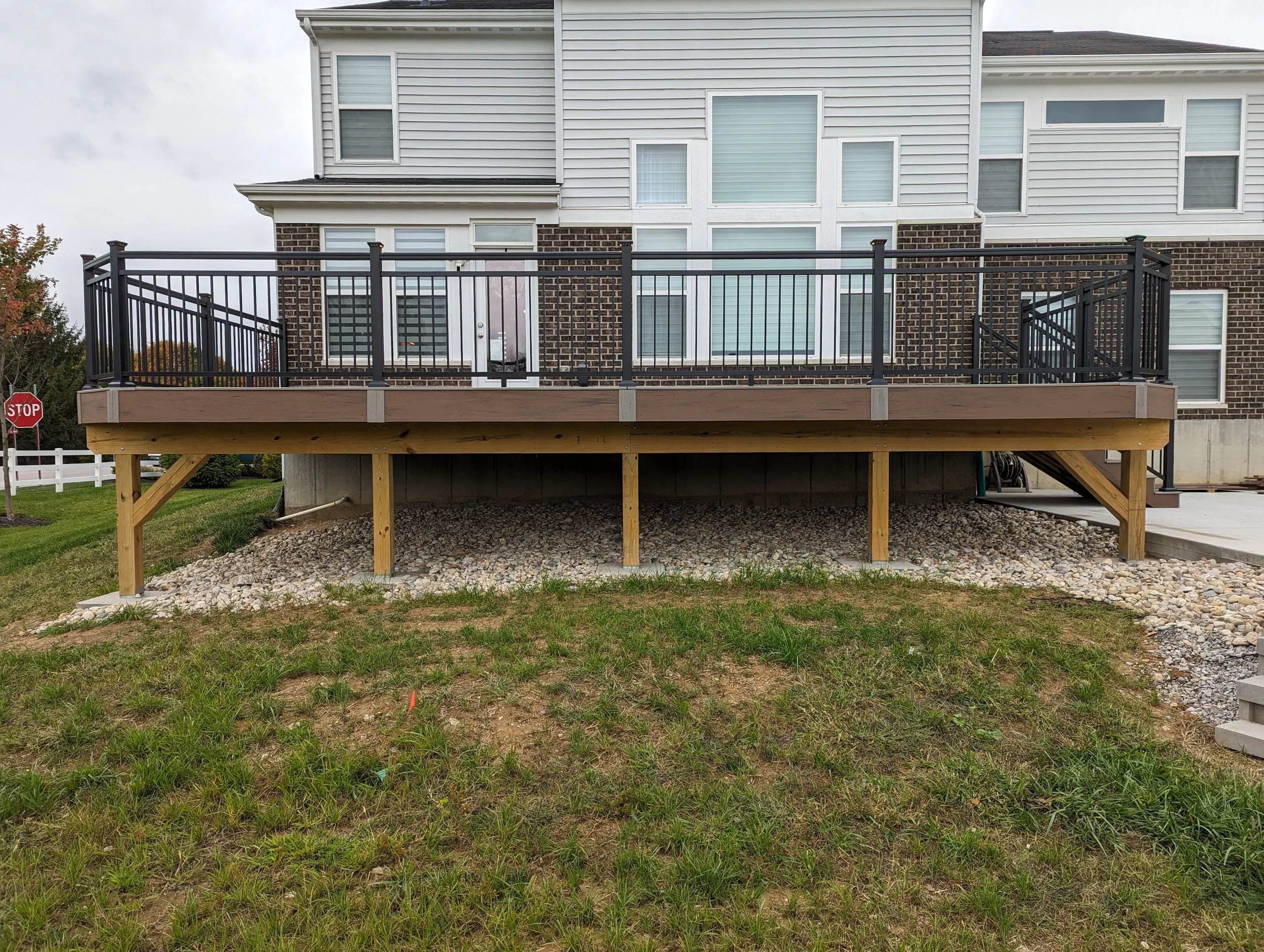 Newly built wooden deck with black metal railing attached to the back of a townhouse.