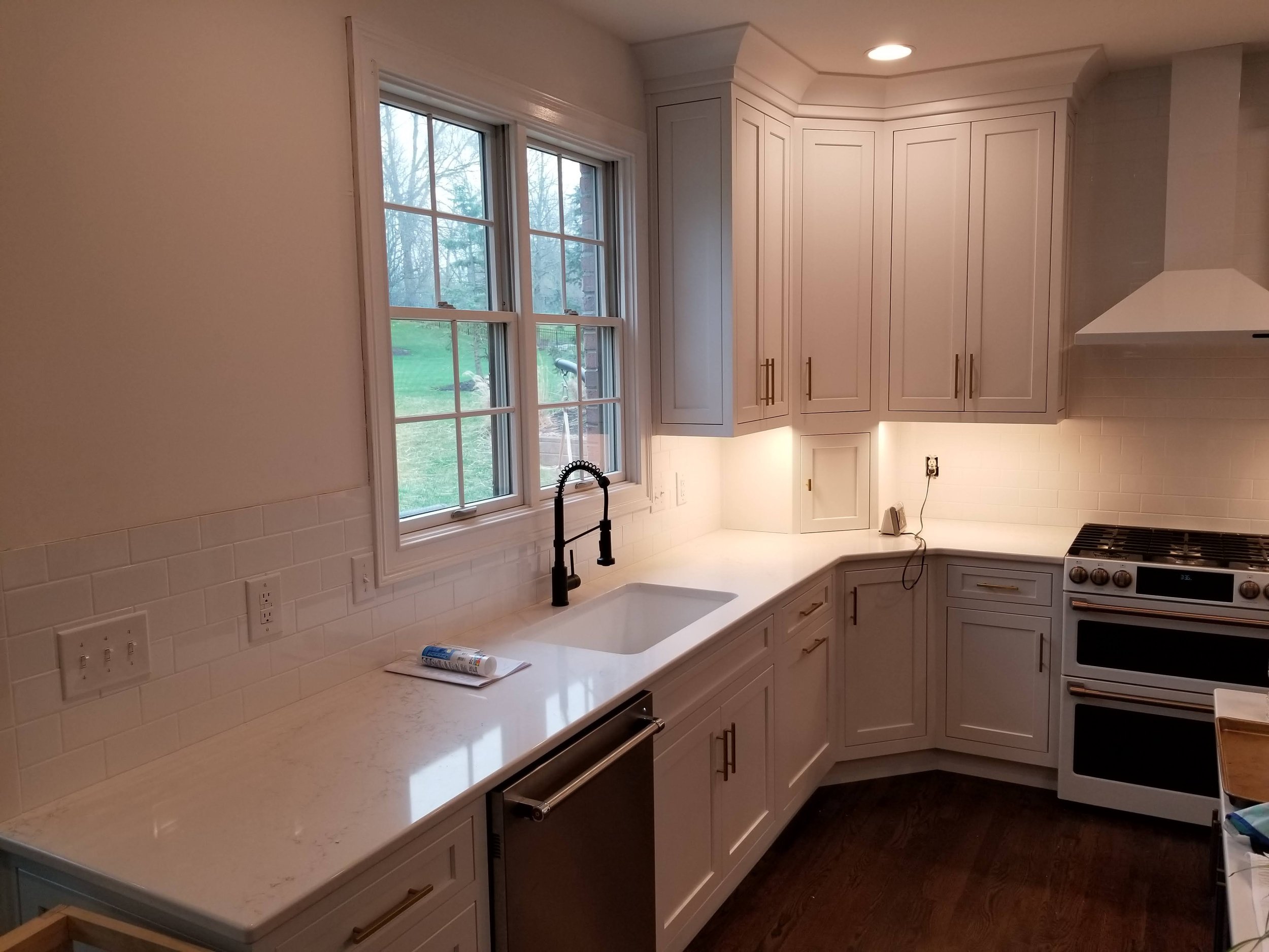 Kitchen with white cabinets, marble countertop, double window above the sink, black faucet, white tile backsplash, stove, and hardwood floors