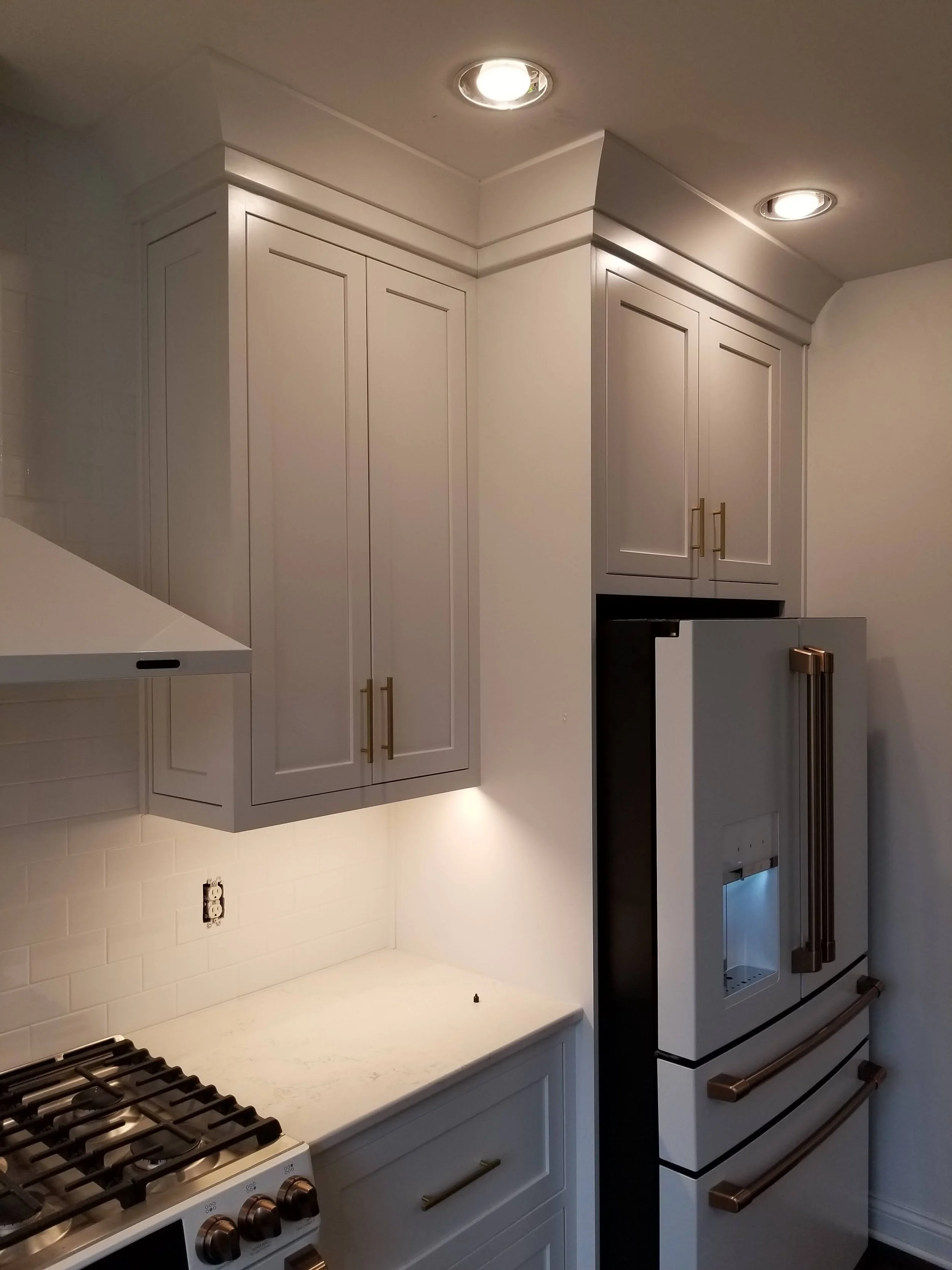 Kitchen with white cabinets, marble countertop, and a white refrigerator with brass handles.