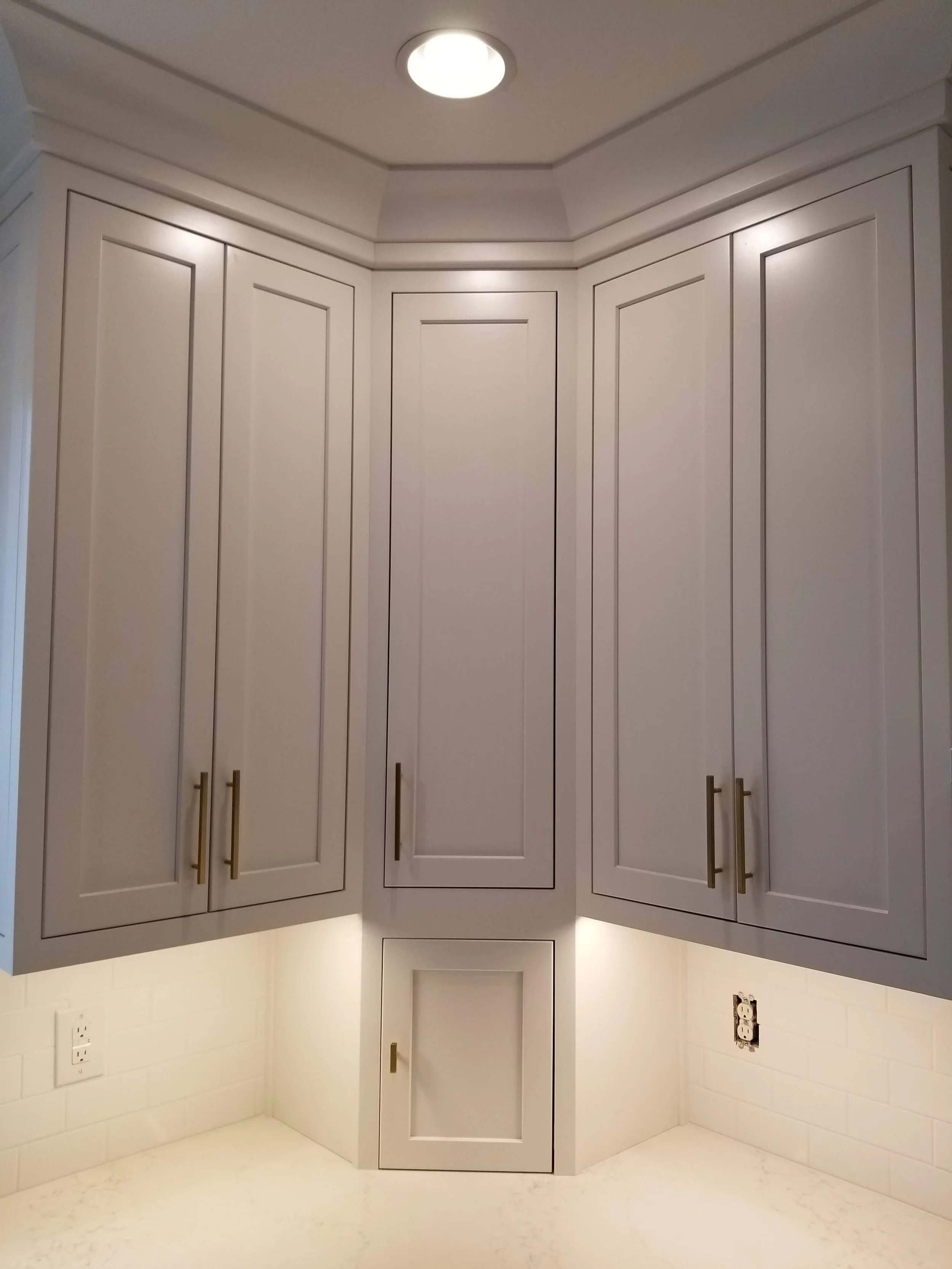 Kitchen corner with white cabinets, gold handles, under-cabinet lighting, and an overhead ceiling light.