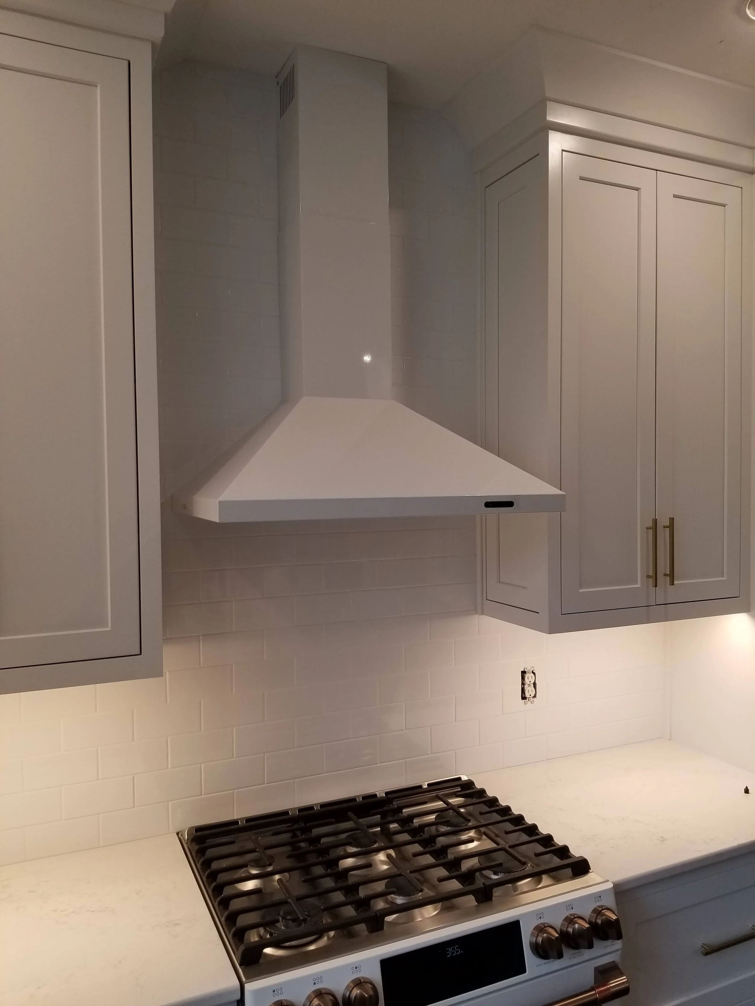 Kitchen with white cabinets, a white range hood, a white countertop, a gas stove, a white subway tile backsplash, and an electrical outlet on the wall.