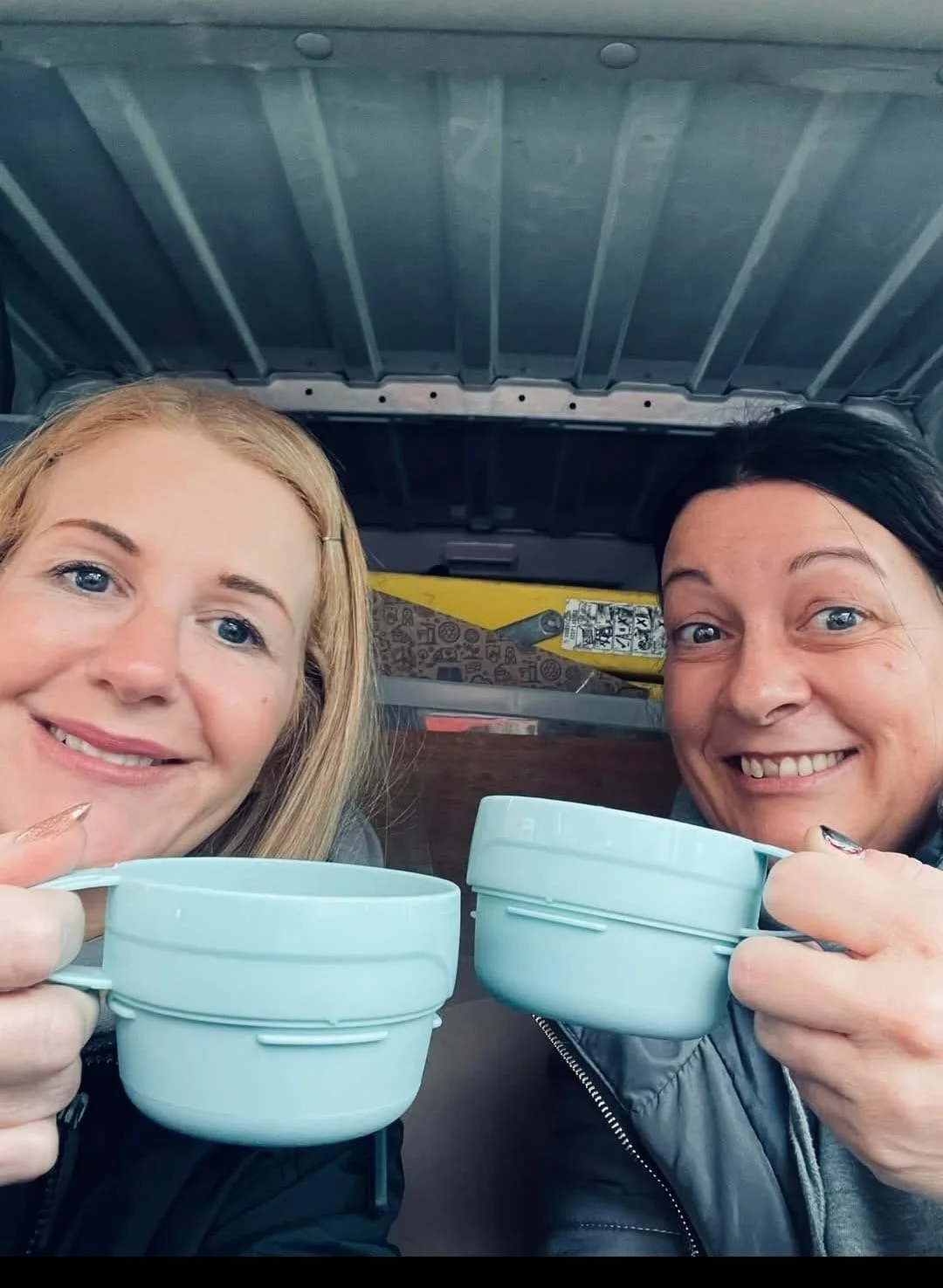 Two women smiling and holding blue mugs, sitting together in a cozy setting.