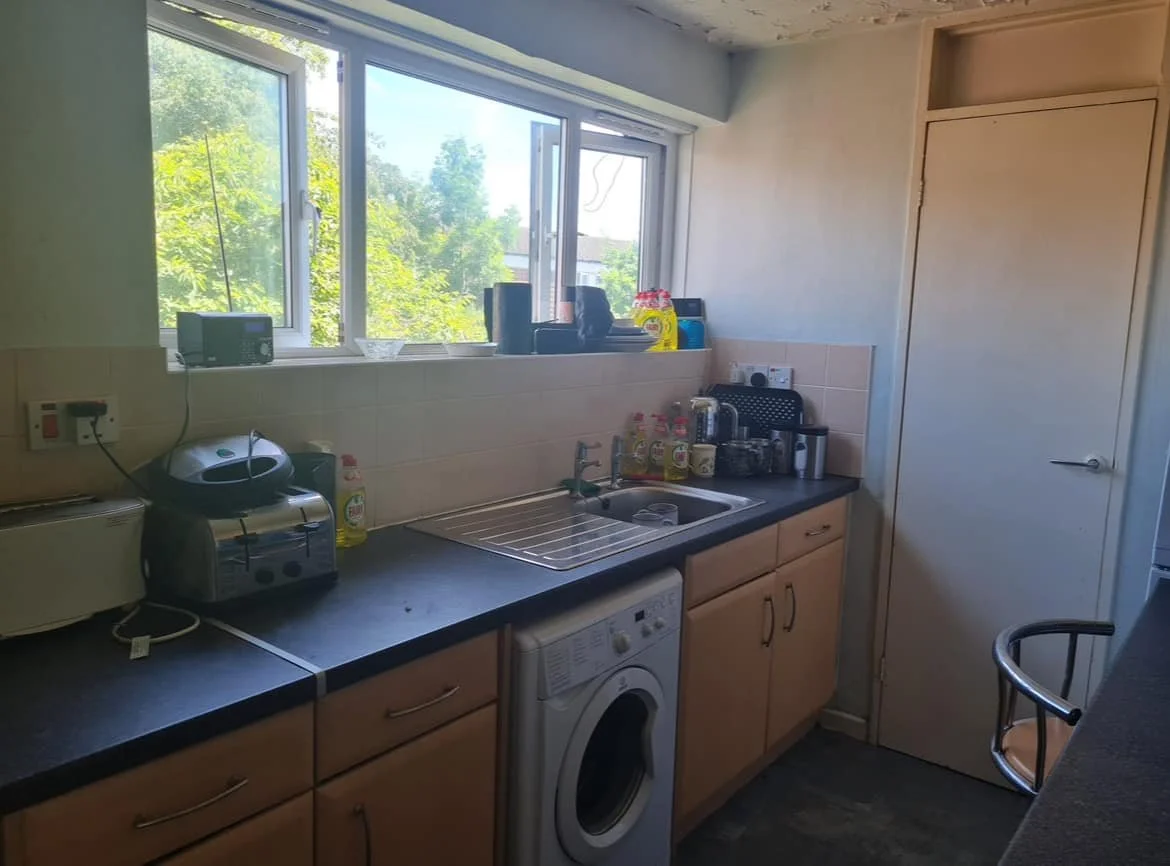 Kitchen with a window, counter with appliances, soap bottles, a sink, and a washing machine underneath the counter.