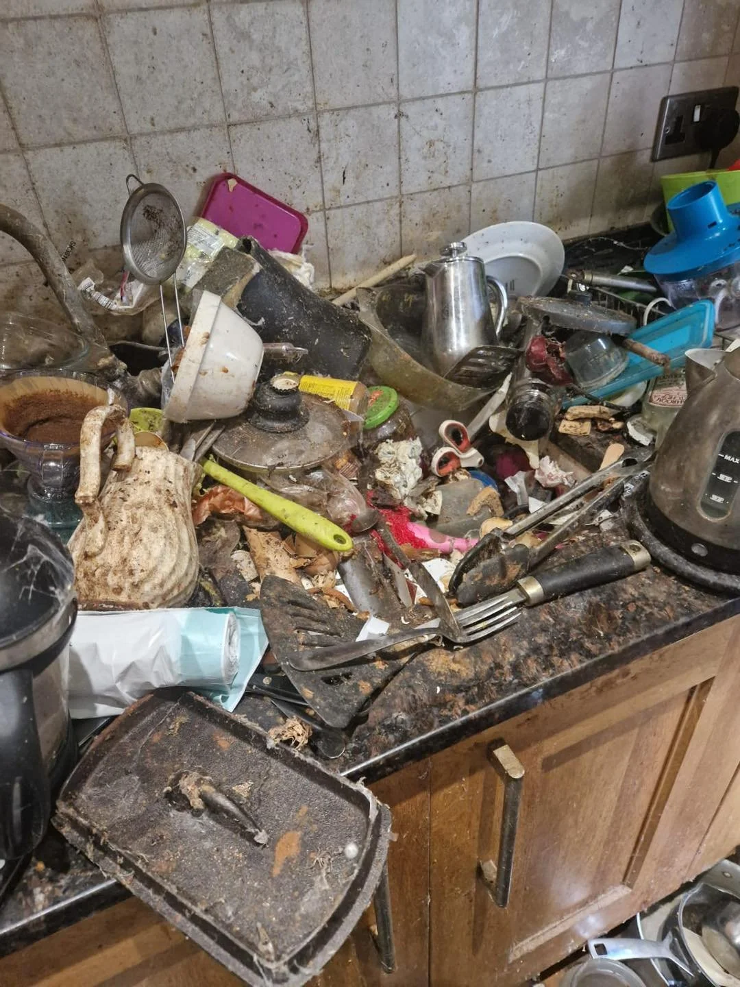 Cluttered and dirty kitchen countertop with dirty dishes, pots, utensils, and debris.