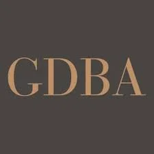 Close-up of a logo with the letters GDBA in beige on a dark background.