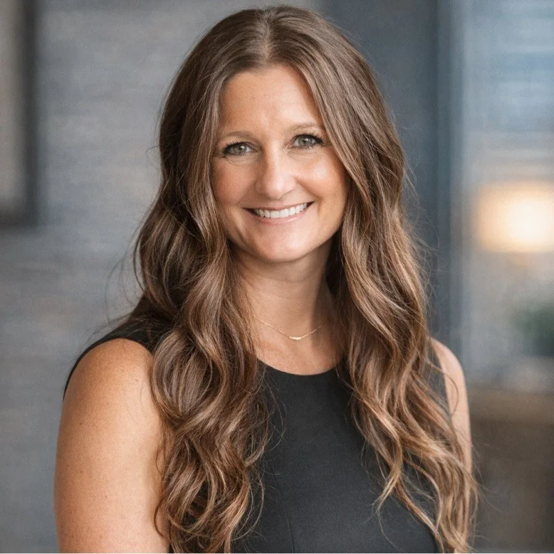 A smiling woman with long, wavy brown hair wearing a black sleeveless top.