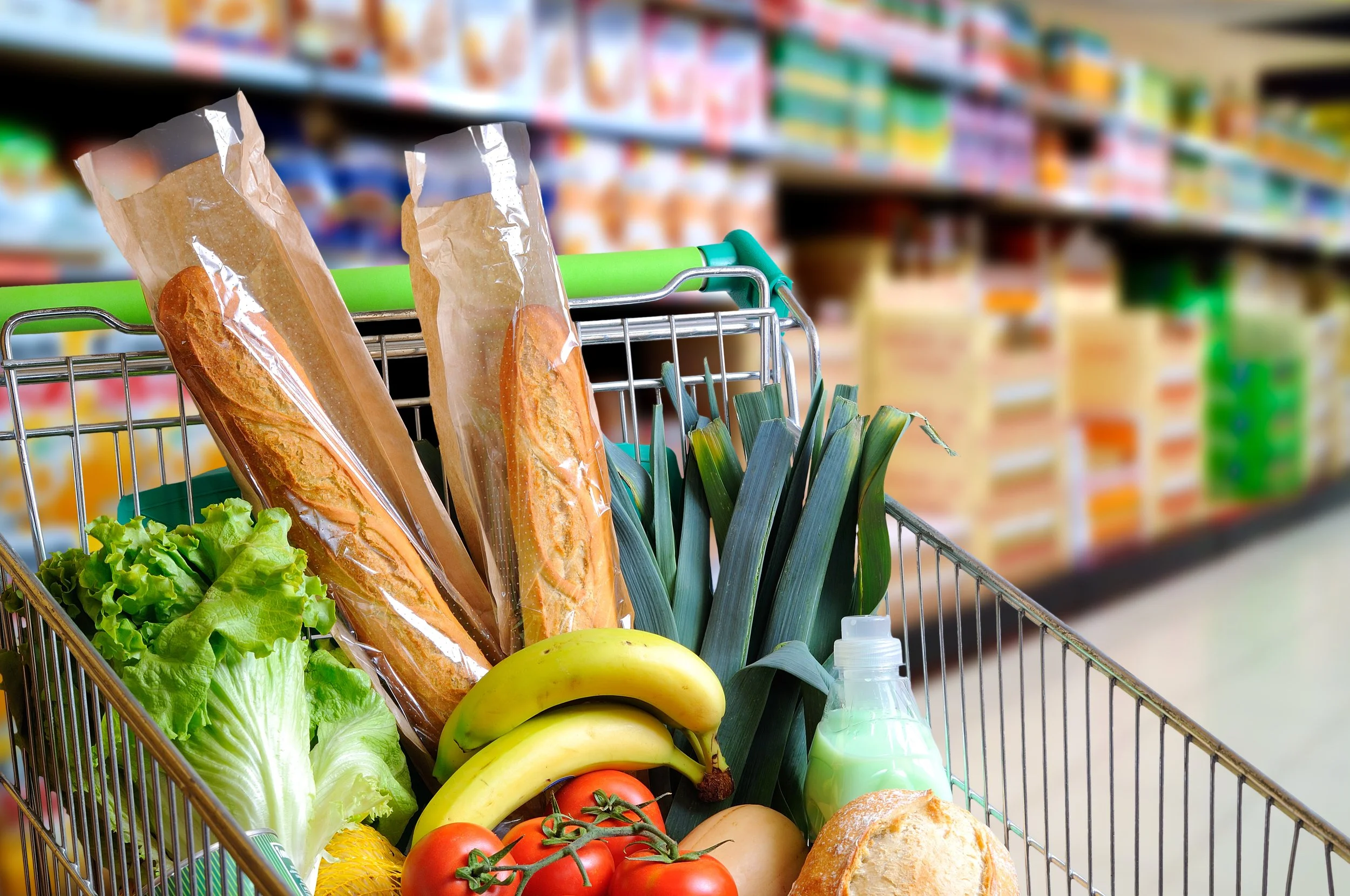 Shopping cart filled with vegetables and bread at grocery store