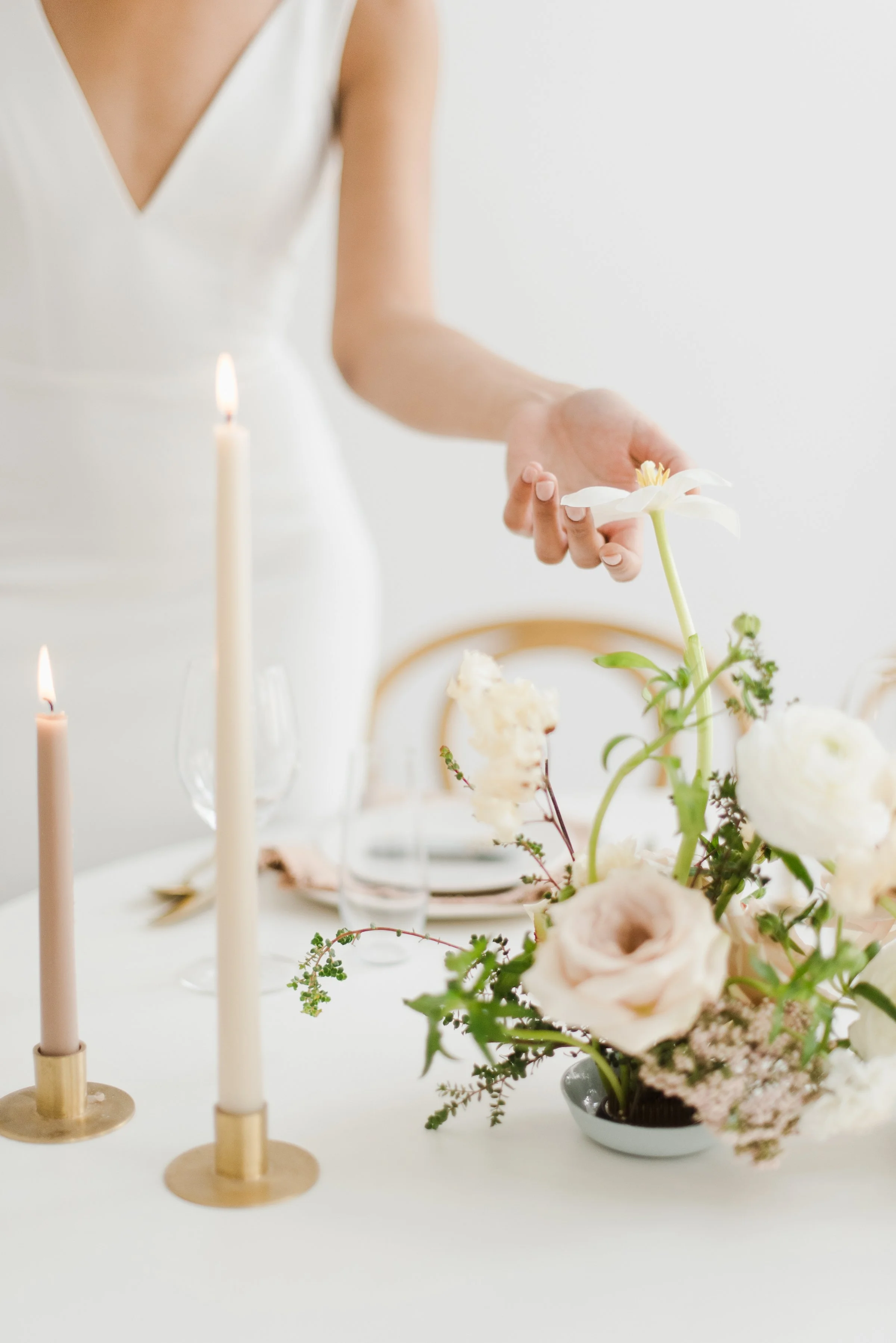 Table de décoration avec des bougies, des fleurs blanches et roses dans un vase, ambiance élégante et minimaliste.