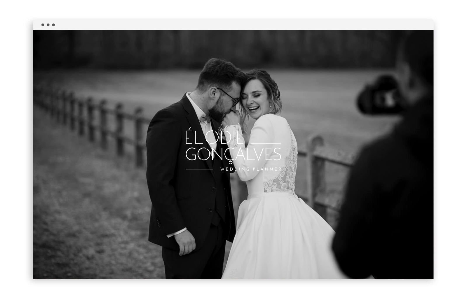 Une photo en noir et blanc d'un couple de mariage souriant et partageant un moment intime lors d'une séance photo en plein air, avec un photographe en arrière-plan