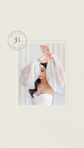 Une femme en robe blanche avec des manches en tulle, levant les bras, dans un décor blanc avec rideaux. Portrait élégant.