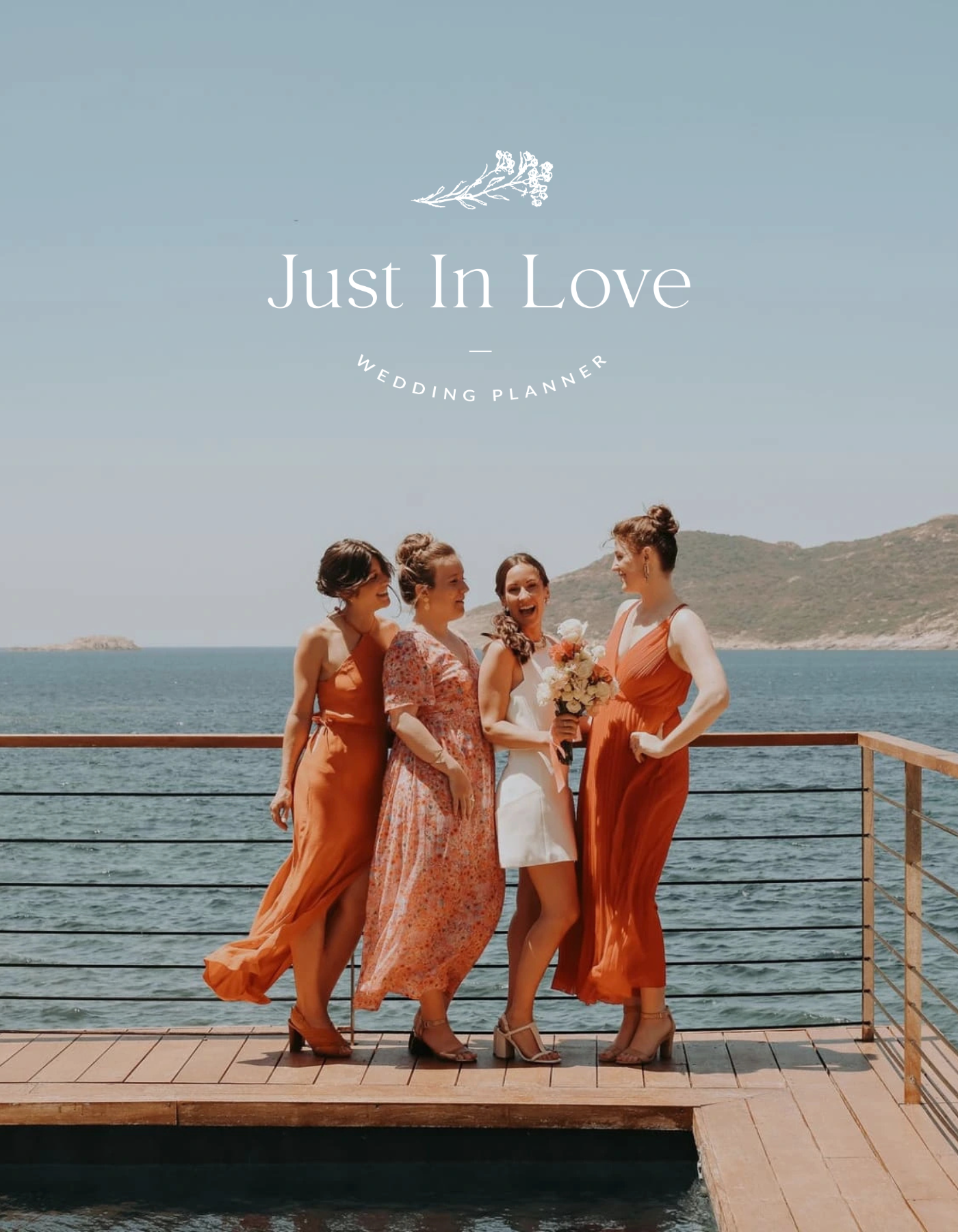 Groupe de cinq femmes en robes d'été de couleurs orange, rose et blanc, discutant et riant sur un pont en bois en bord de mer avec des montagnes en arrière-plan, lors d'un mariage.