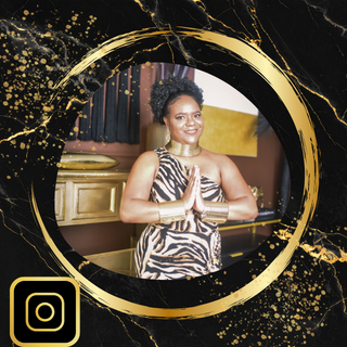A woman with curly hair in a zebra-print dress, standing indoors with her hands in a prayer position, smiling.