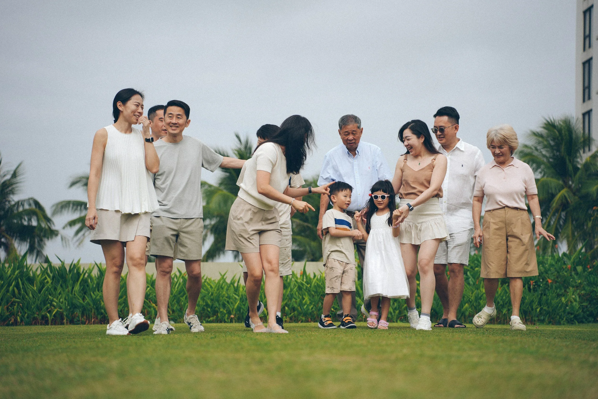 A group of people, including children and adults, enjoying a walk and having fun outdoors on a grassy field with palm trees in the background.