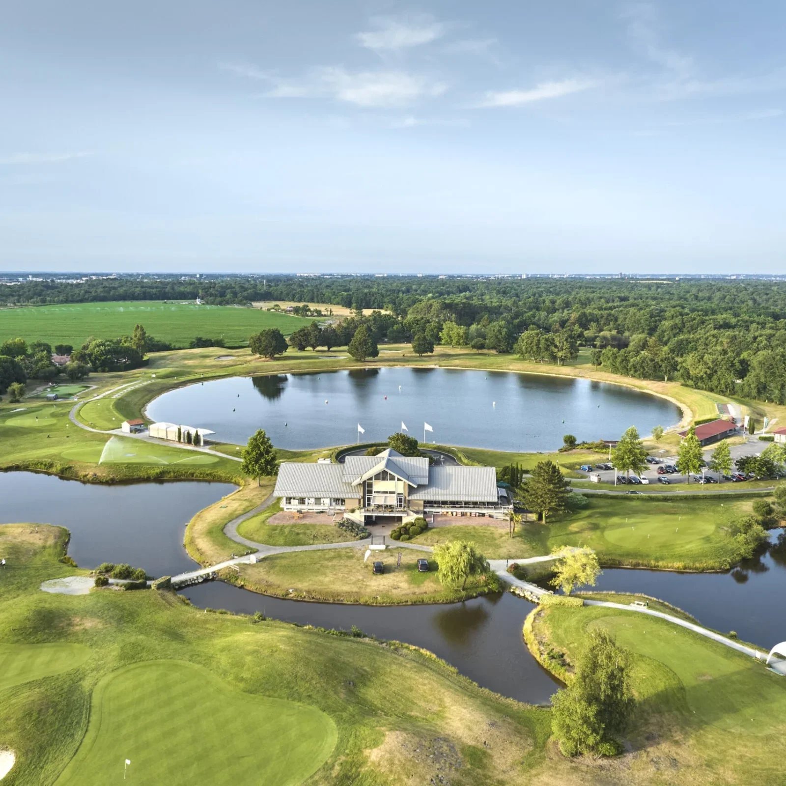 Aerial view of a golf course with a clubhouse, multiple lakes, parks, and trees.