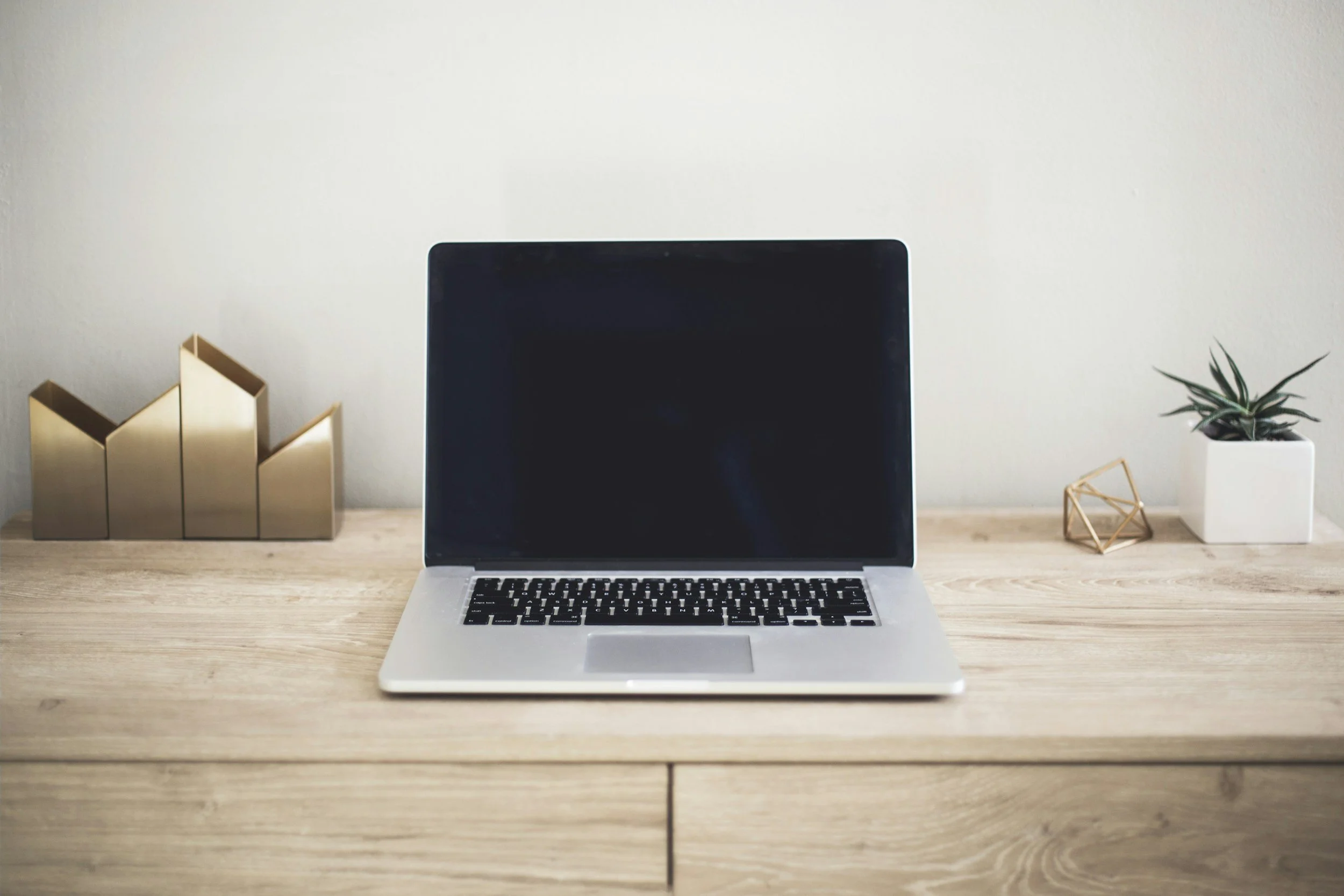 A laptop on a wooden desk with decorative items including gold bookend shapes, a small potted plant, and a geometric ornament.