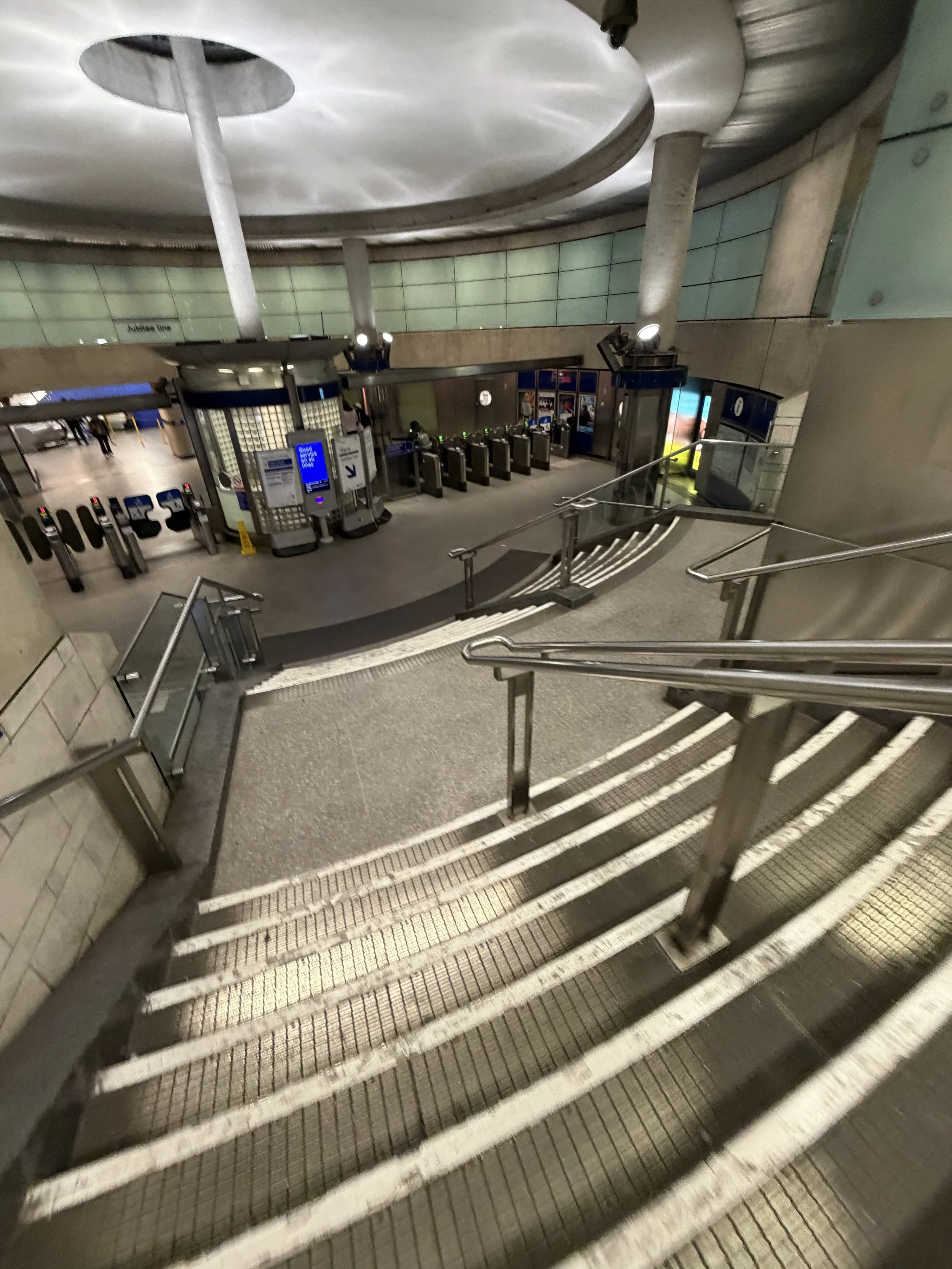 Escalator leading down to an underground subway station with ticket barriers and turnstiles.