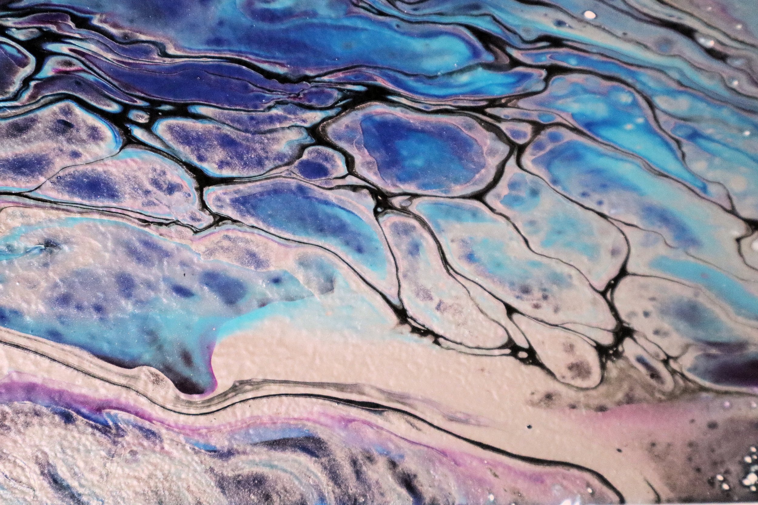 A close-up of an abstract artwork with swirling patterns in shades of blue, purple, black, and hints of pink and white.
