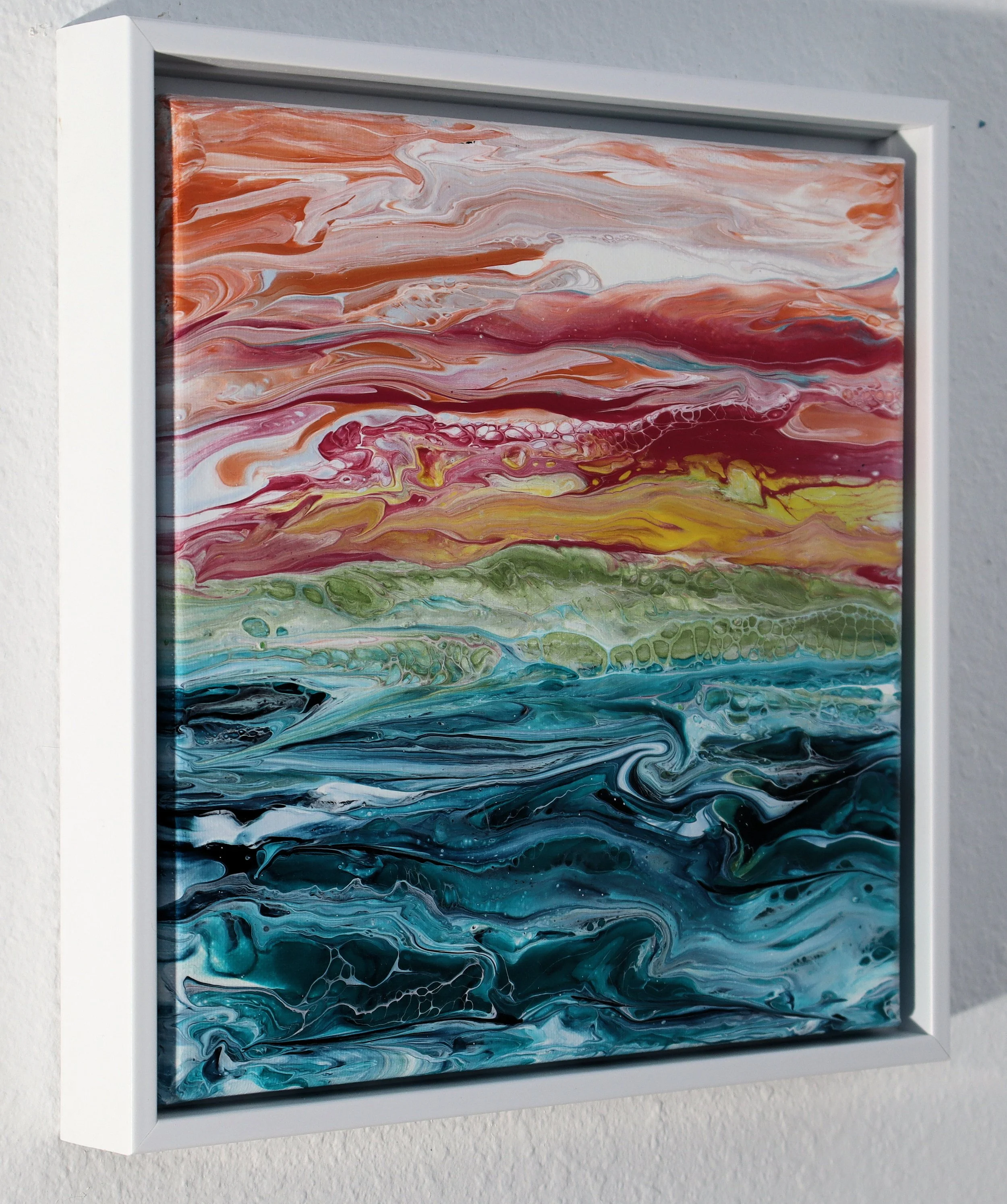 Abstract marbled painting with swirls of orange, pink, yellow, green, blue, and black, framed in white, mounted on a wall.
