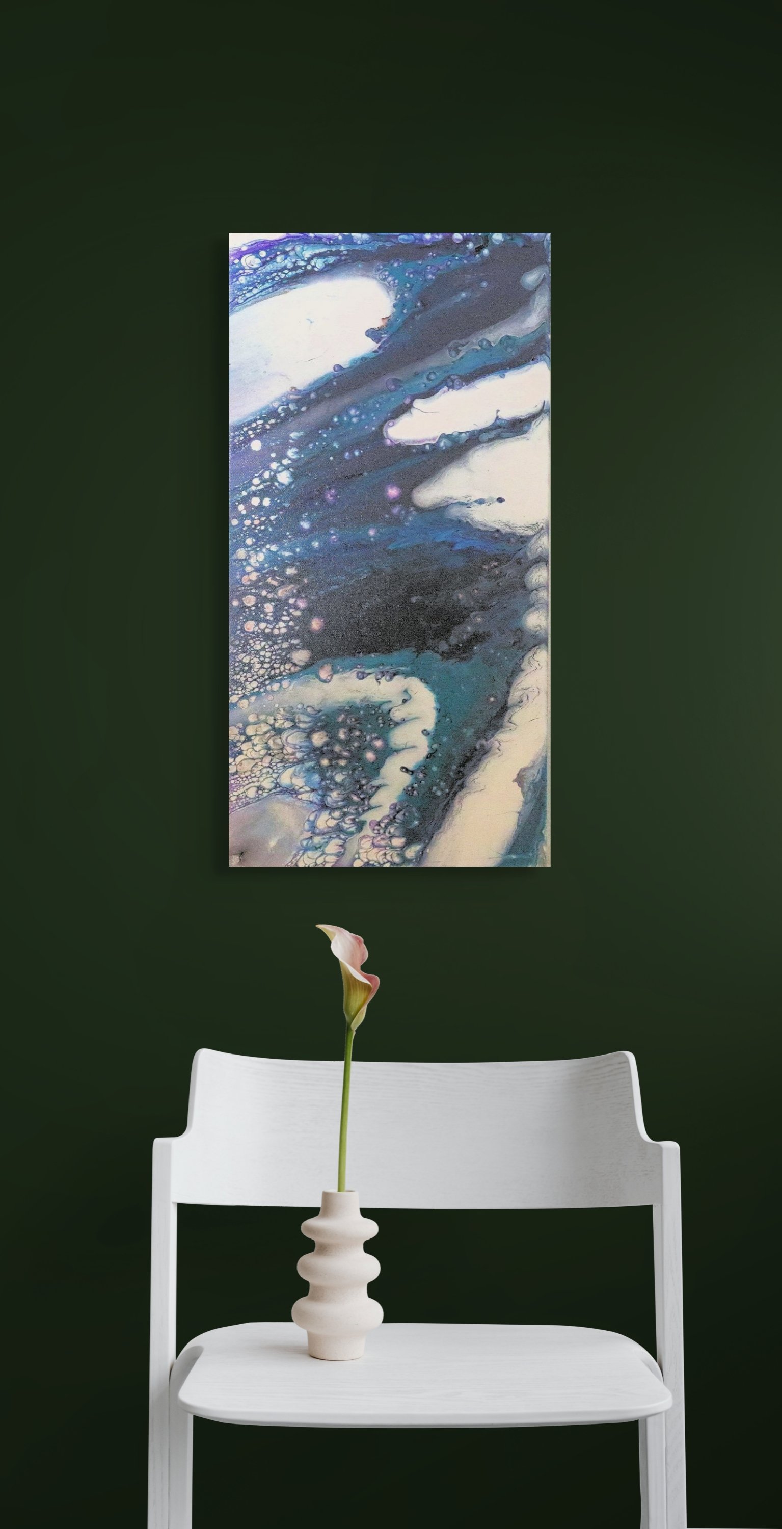 A white chair with a white vase holding a single pink calla lily flower. The background is a dark green wall with a large abstract painting in shades of blue, white, black, and purple hanging behind the chair.