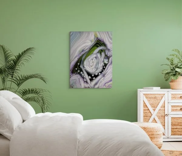 A bedroom with a green wall, a white bed, a potted plant, a white cabinet with rattan drawers, and a colorful abstract painting on the wall.