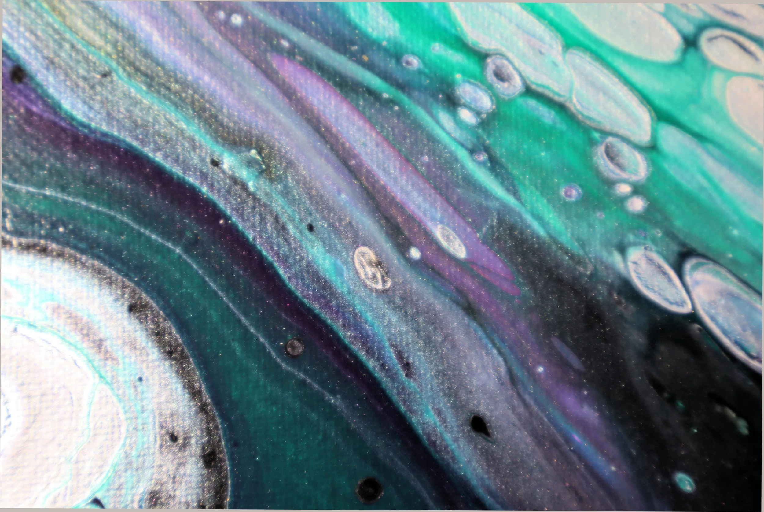 Close-up of an iridescent, colorful surface with metallic hues of purple, green, blue, and hints of gold, featuring circular patterns and textures.