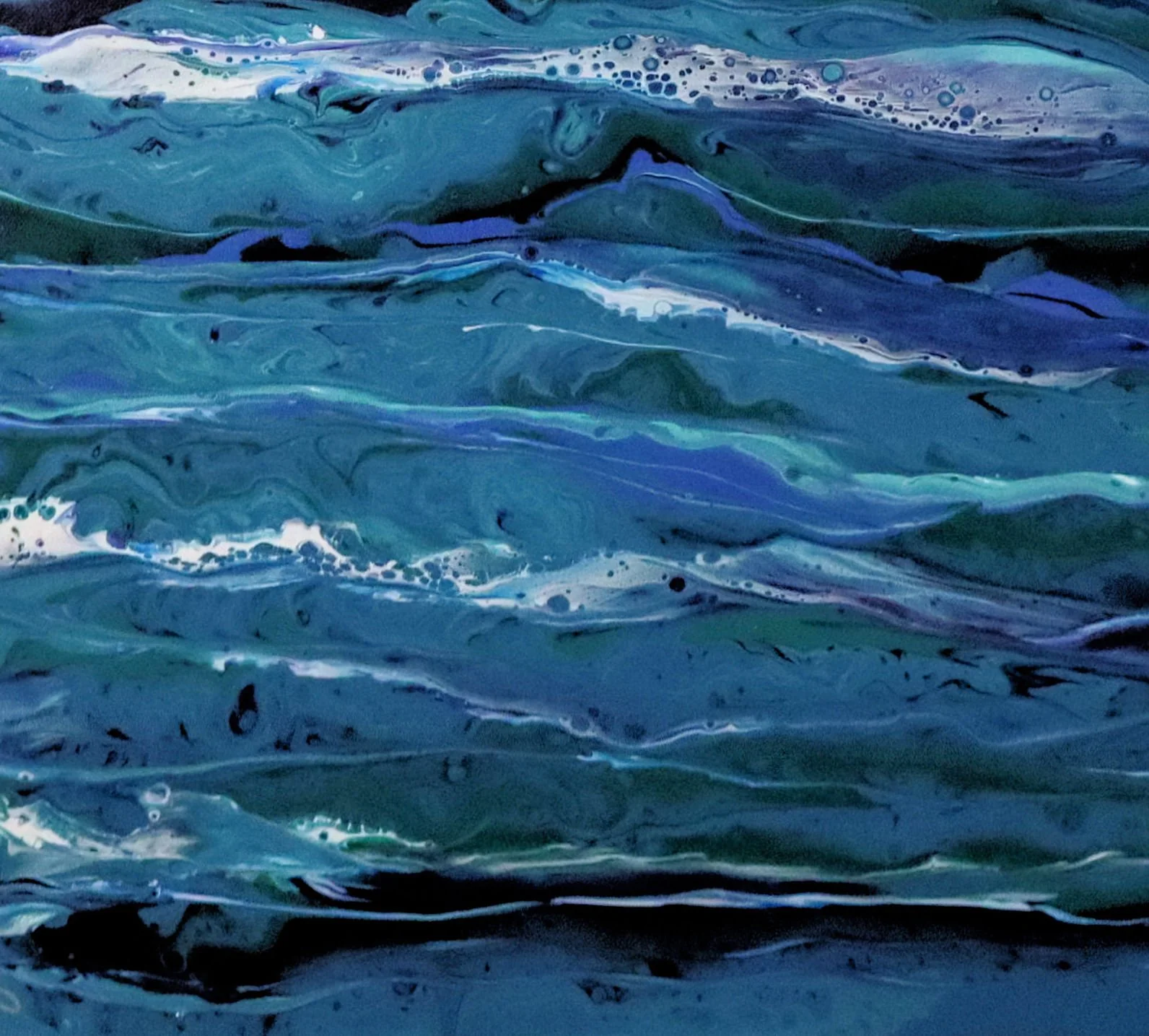 Close-up view of swirling, abstract blue and green watercolor paint on paper.