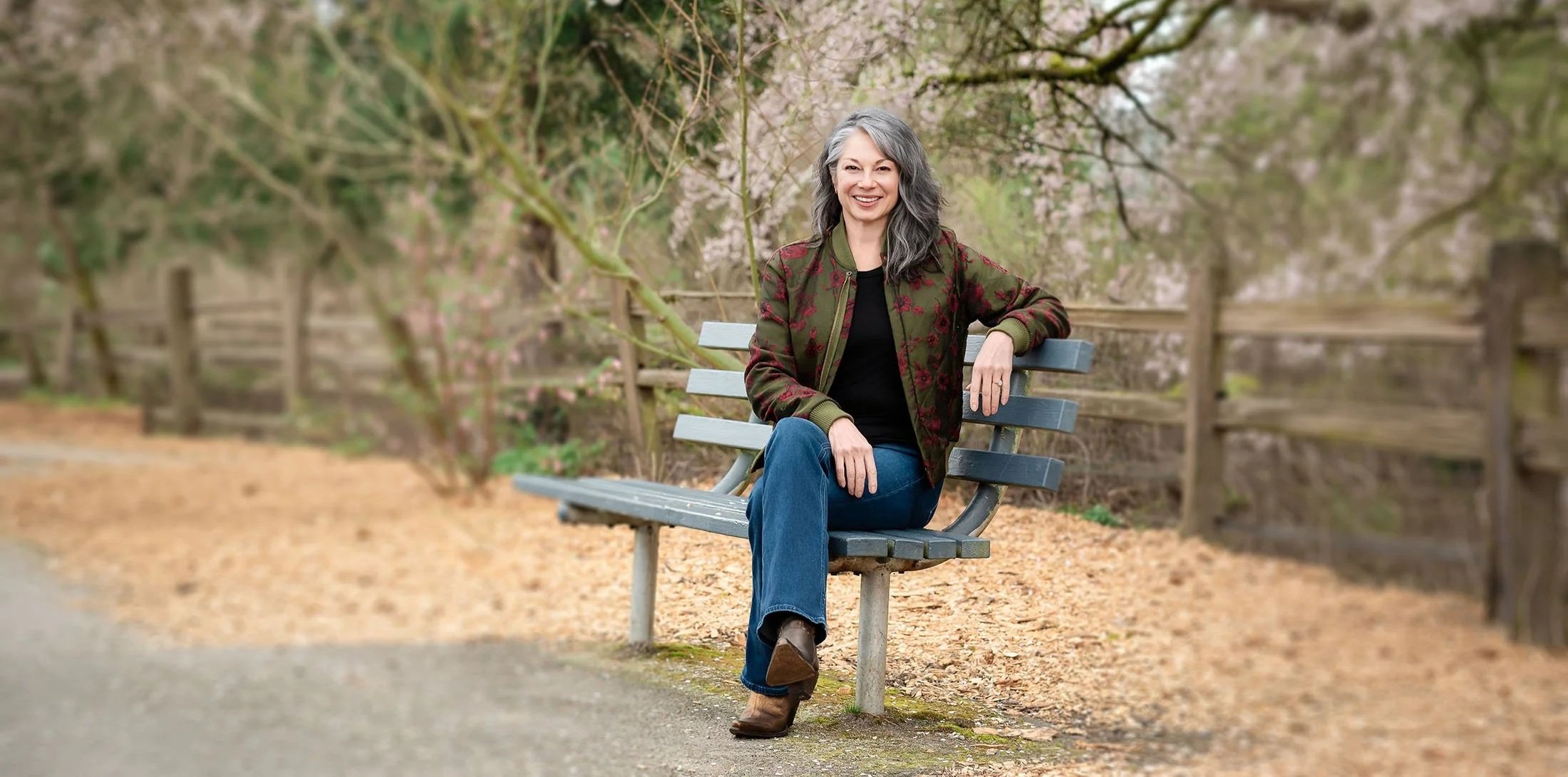 Kellie Torres sitting on a park bench surrounded by blooming trees.