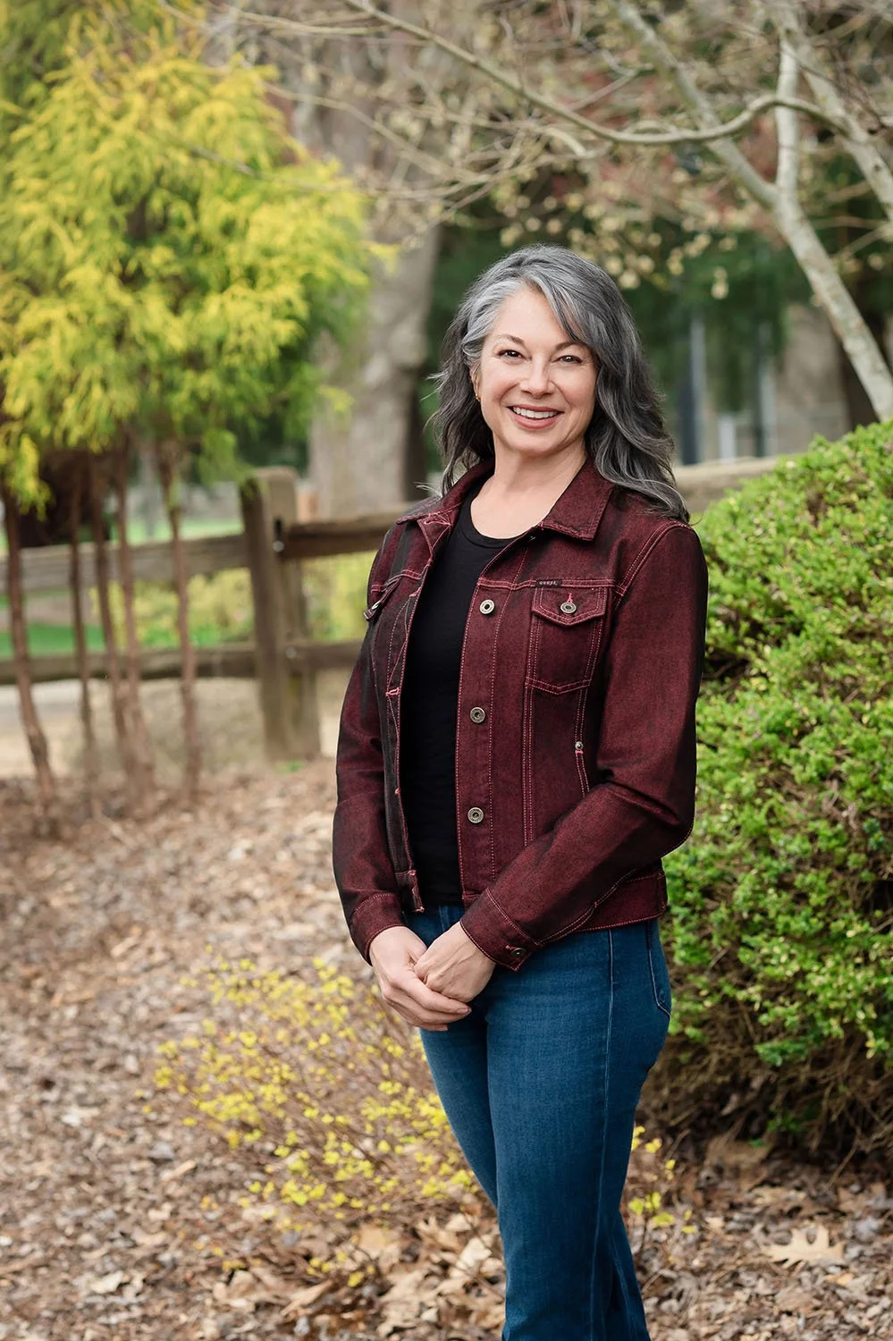 Kellie Torres standing outdoors on a dirt path in a park with trees and bushes in the background.