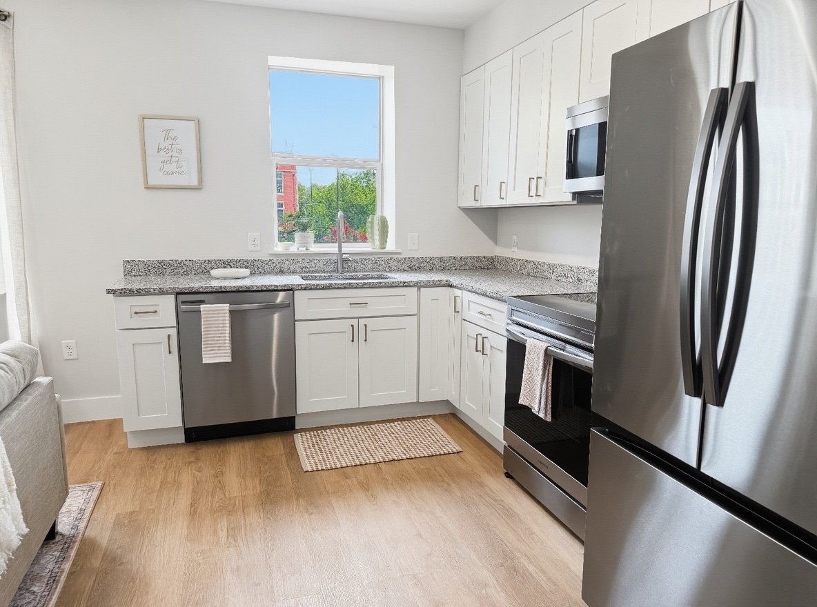 Modern kitchen with white cabinets, stainless steel appliances, granite countertops, and a window above the sink showing greenery outside.