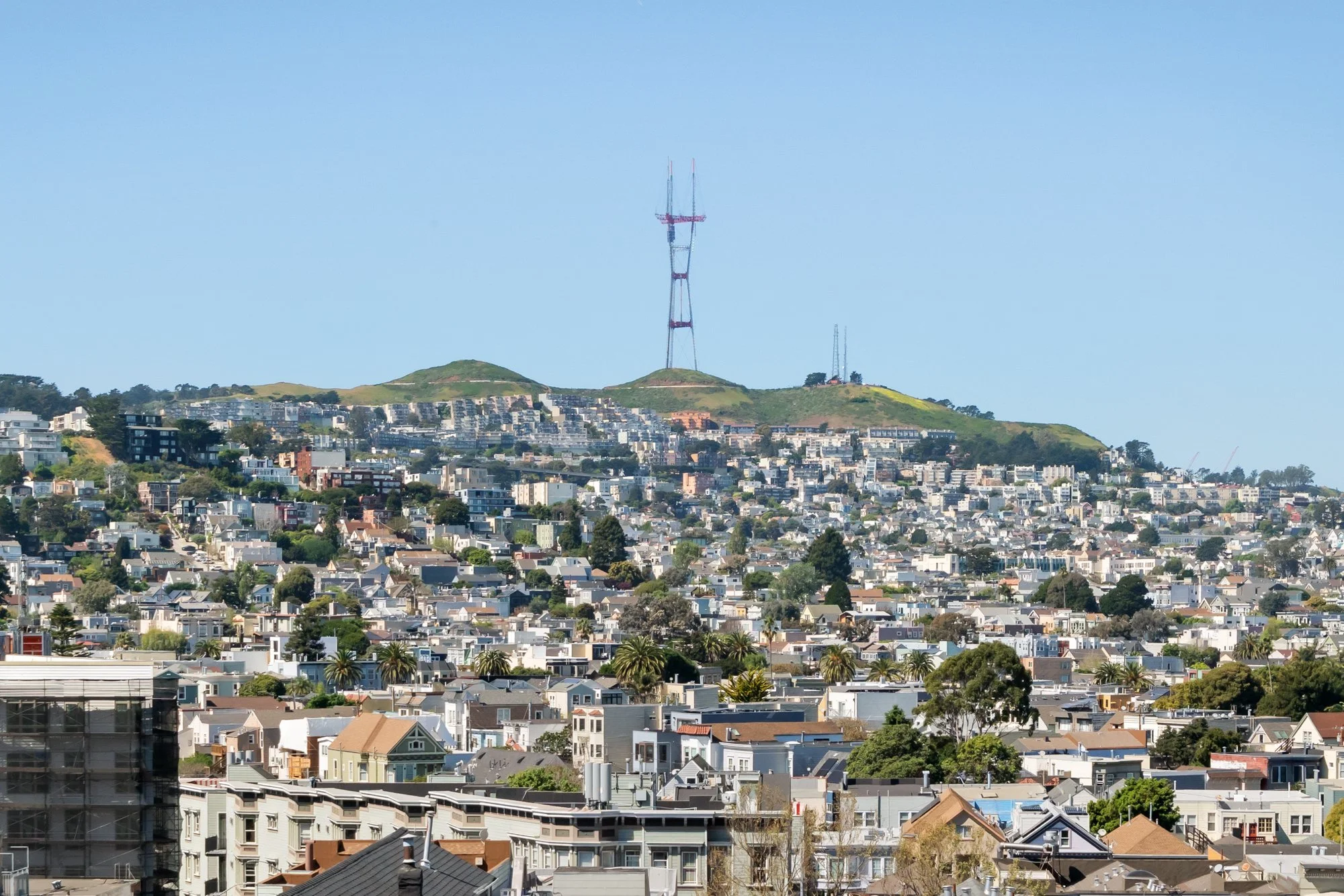 A cityscape of San Francisco with residential buildings, hills, and the iconic Sutro Tower against a clear blue sky.