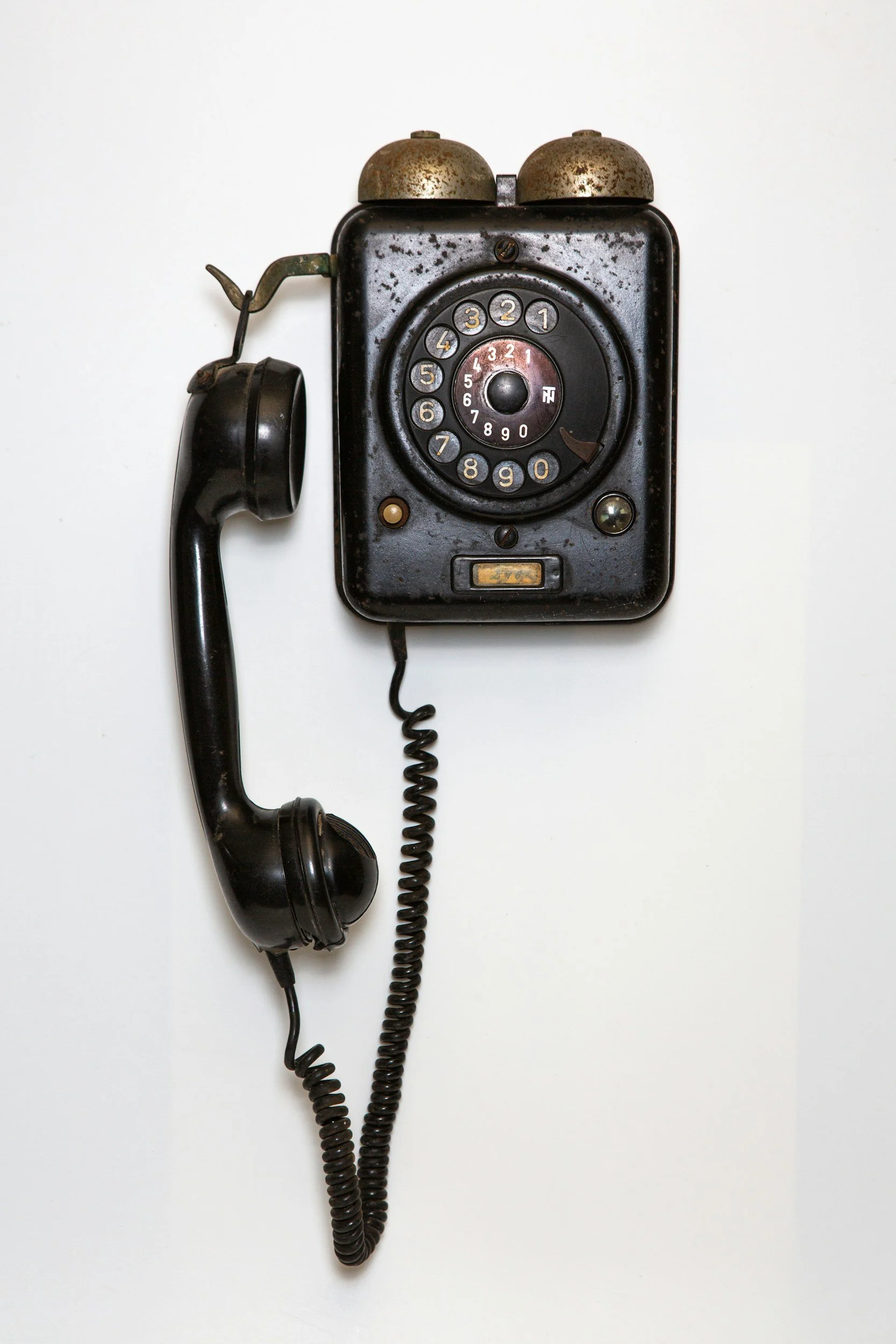 An old black rotary dial telephone mounted on a white wall.