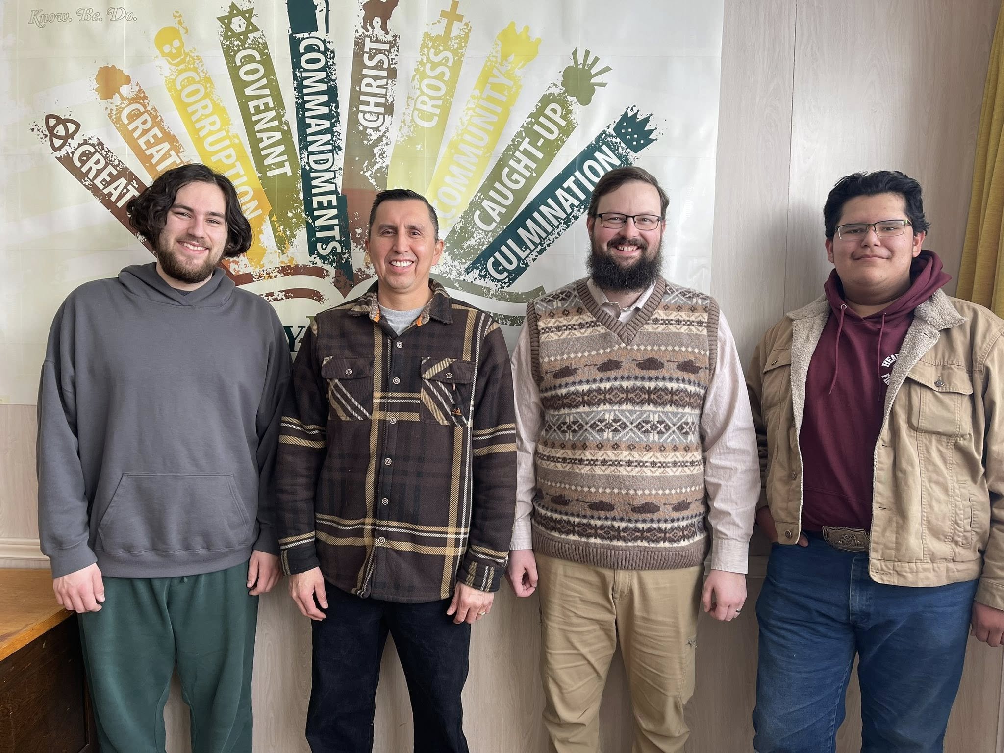 Four men standing side by side in front of a wall, smiling at the camera.