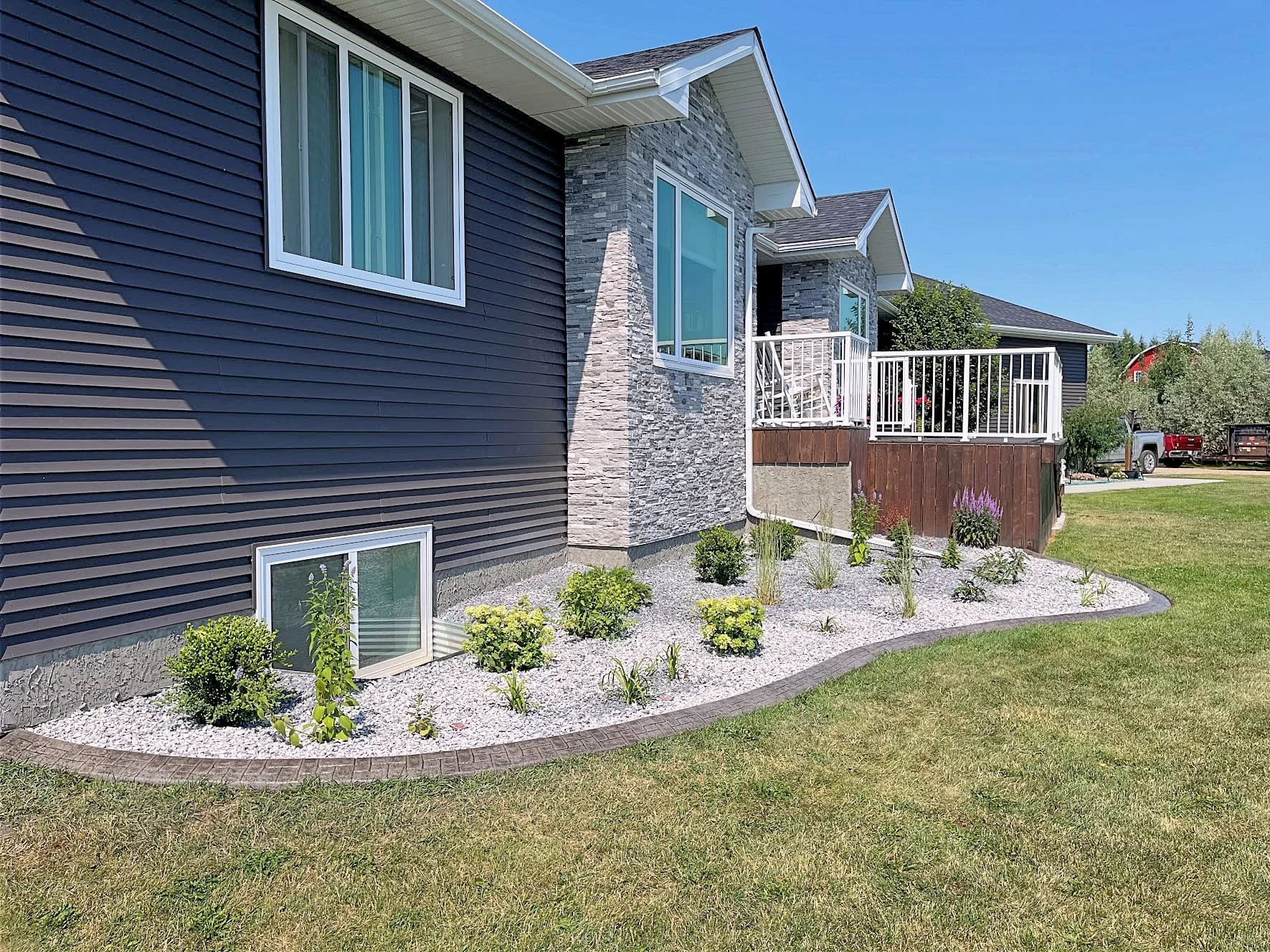 A house with navy blue siding, white-framed windows, a stone accent wall, and a small front yard with landscaped plants and white gravel.