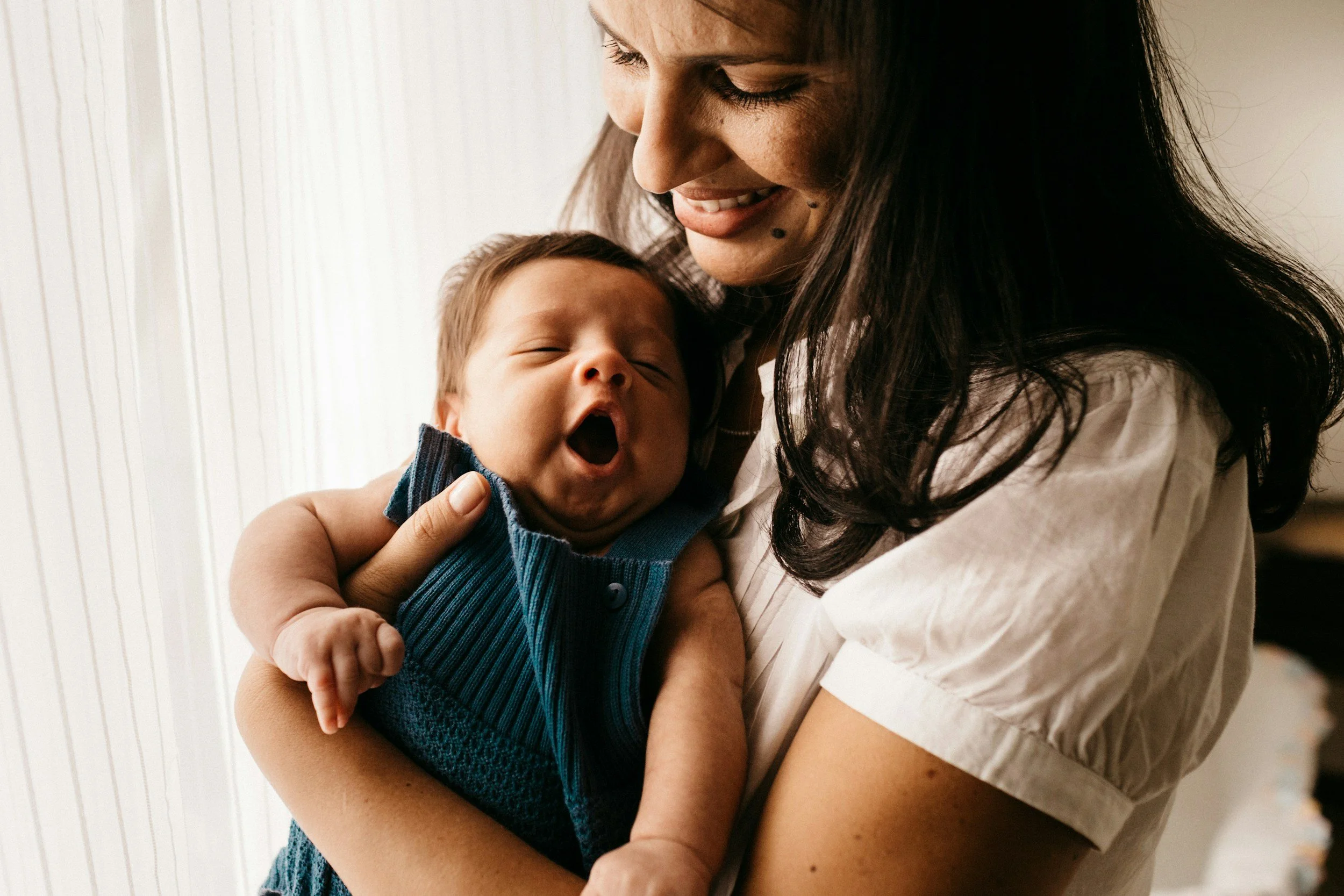 A woman holding a yawning baby in her arms.