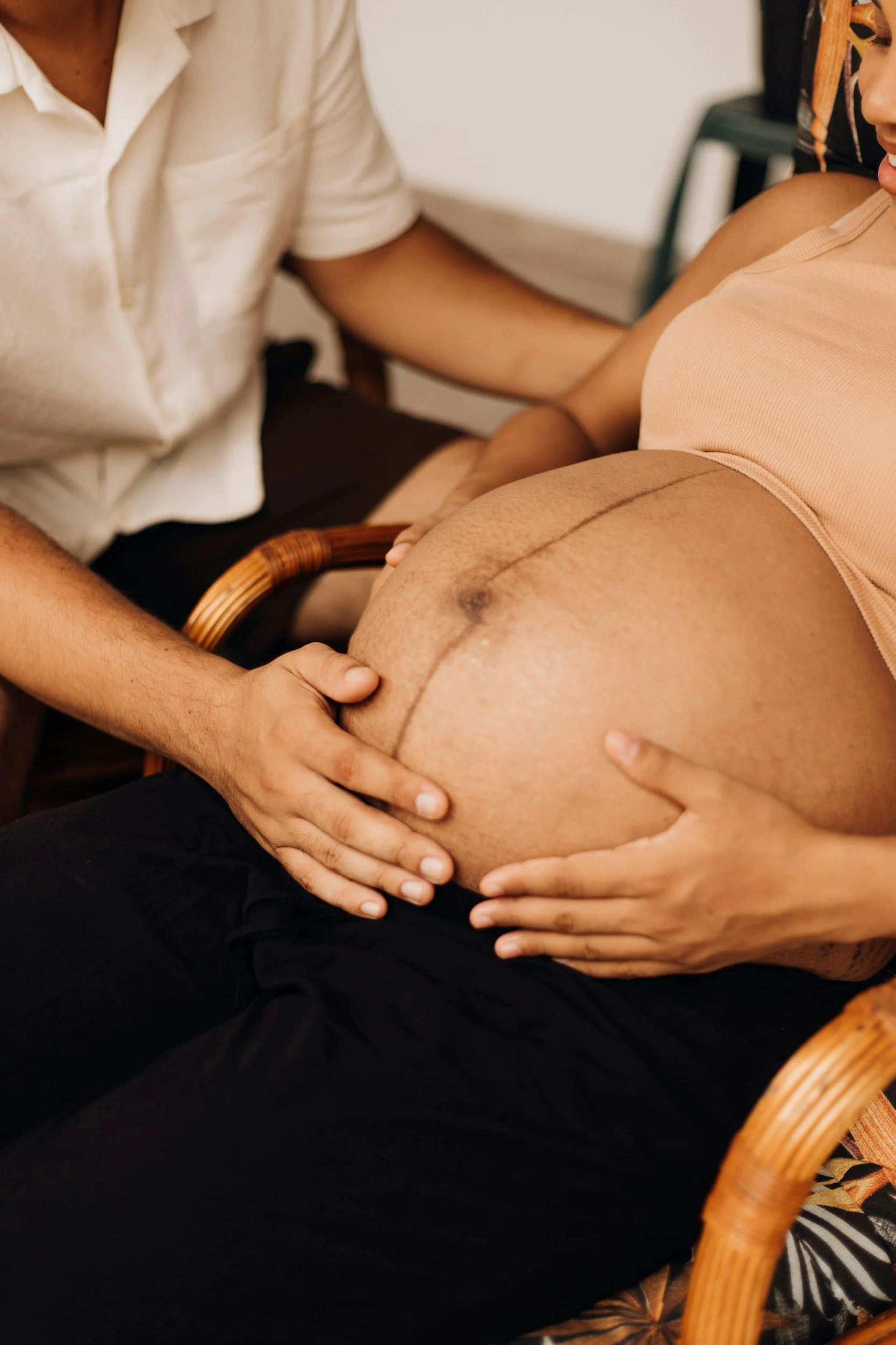 Person cradling a pregnant woman's belly, with hands gently supporting and touching it, in a cozy indoor setting.