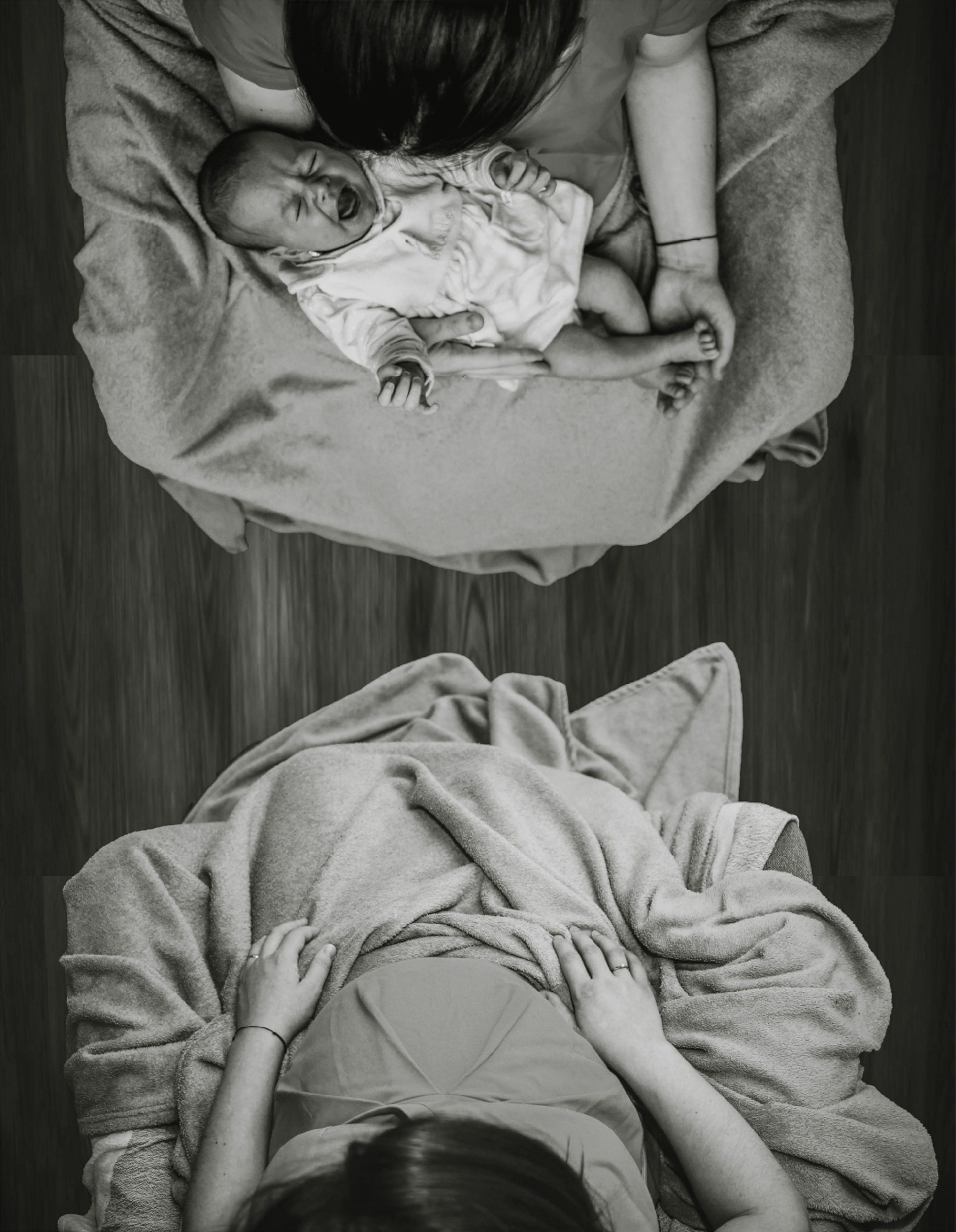 A woman holding a crying baby on a blanket, viewed from above.