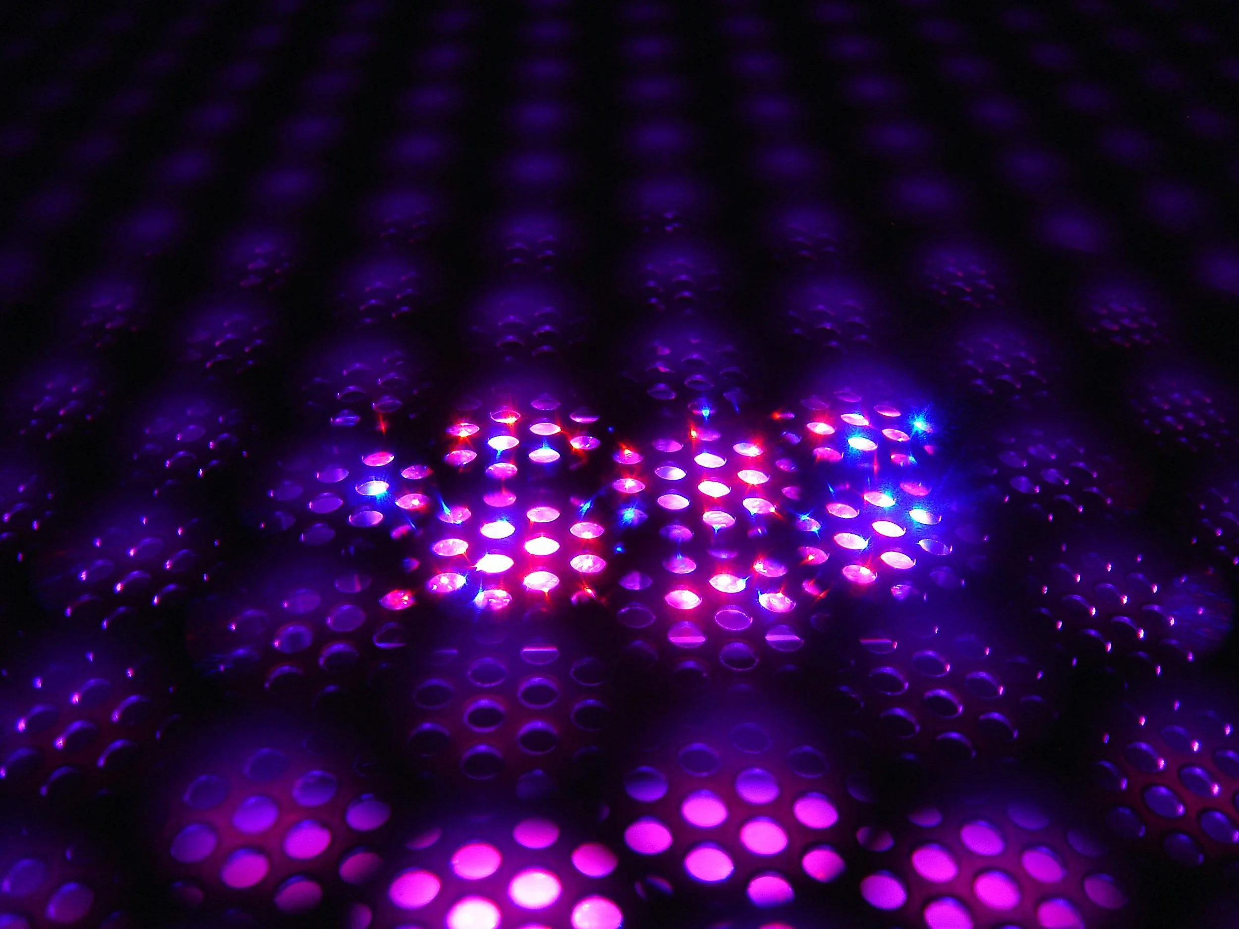 Close-up of a surface with numerous glowing, colorful dots in purple, pink, and blue hues, creating an abstract, futuristic pattern.