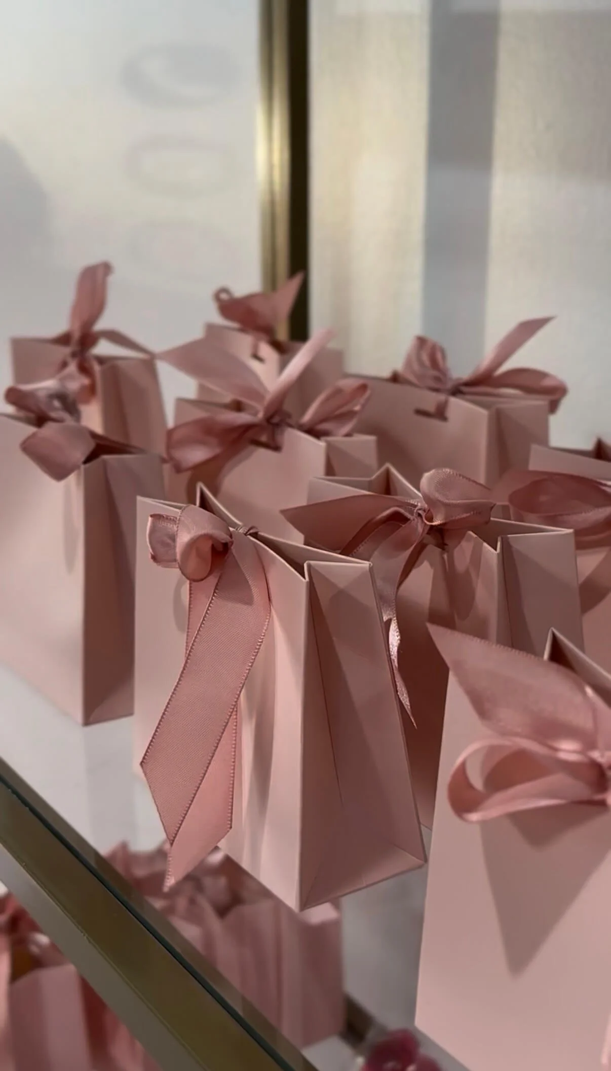 Small pink gift boxes with pink ribbons on a glass surface.