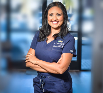 A woman in navy scrubs smiling with arms crossed, standing in front of a blurred background.
