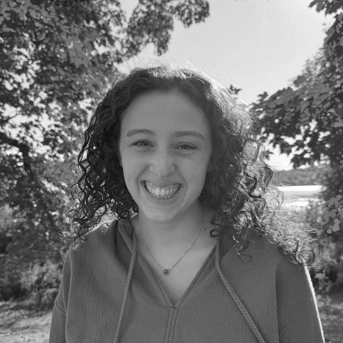 A young woman with curly hair smiling outdoors on a sunny day.