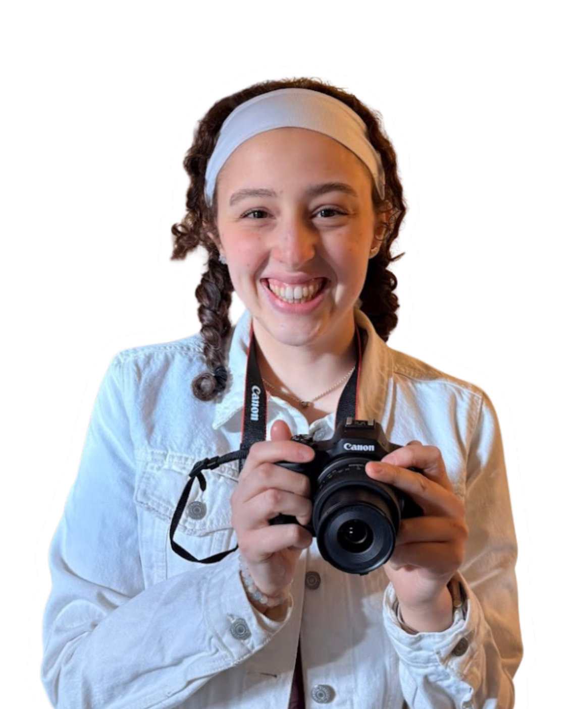 A young woman with curly brown hair wearing a white headband and a white button-up shirt, holding a Canon camera and smiling at the camera.