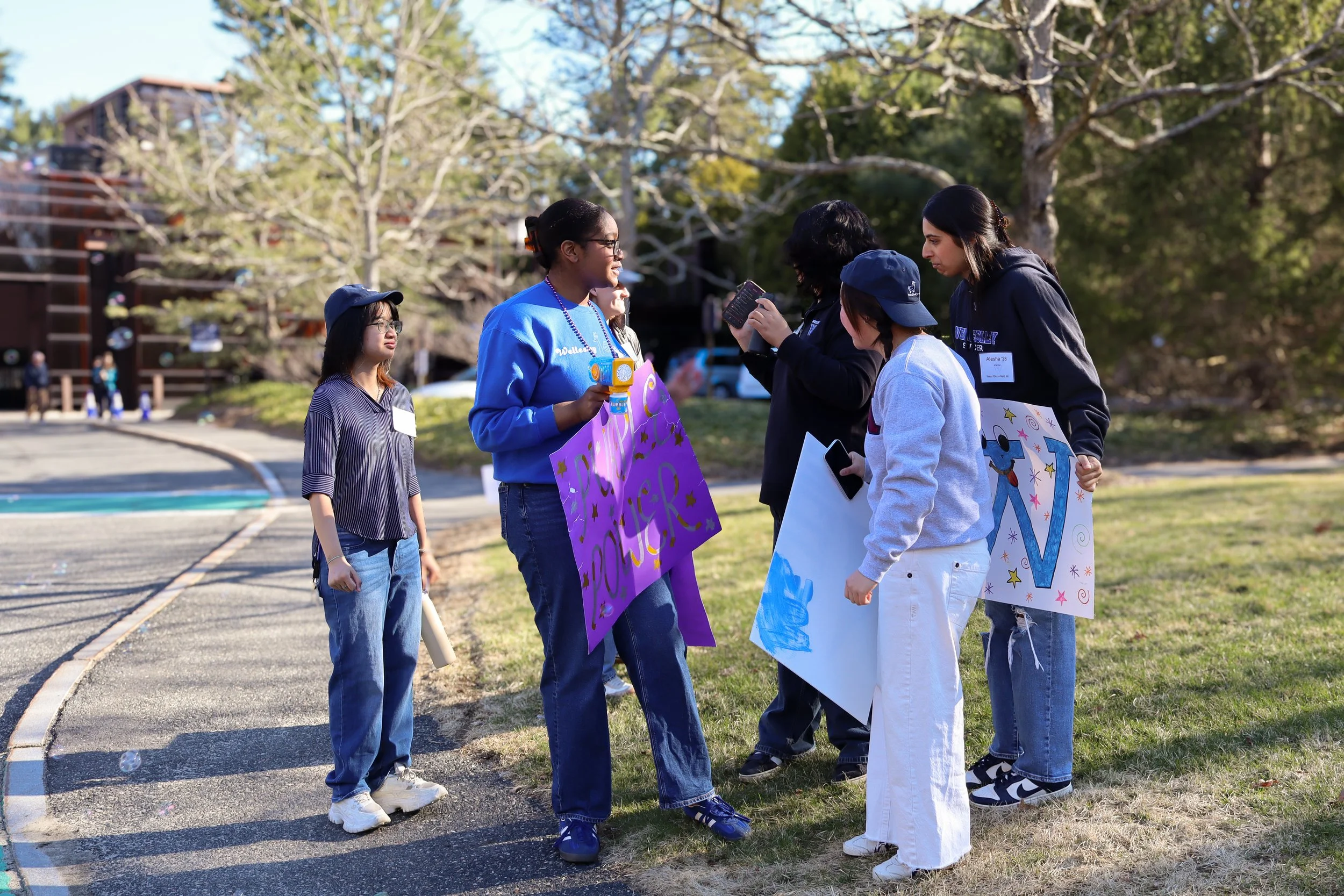 A group of young women participating in a daytime outdoor protest or demonstration, holding colorful posters and signs.