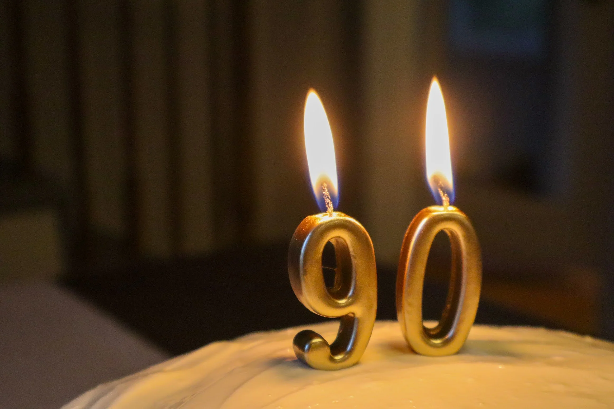 Close-up of two golden menorah candles with flames burning during Hanukkah, on a reflective surface with a dark blurred background.