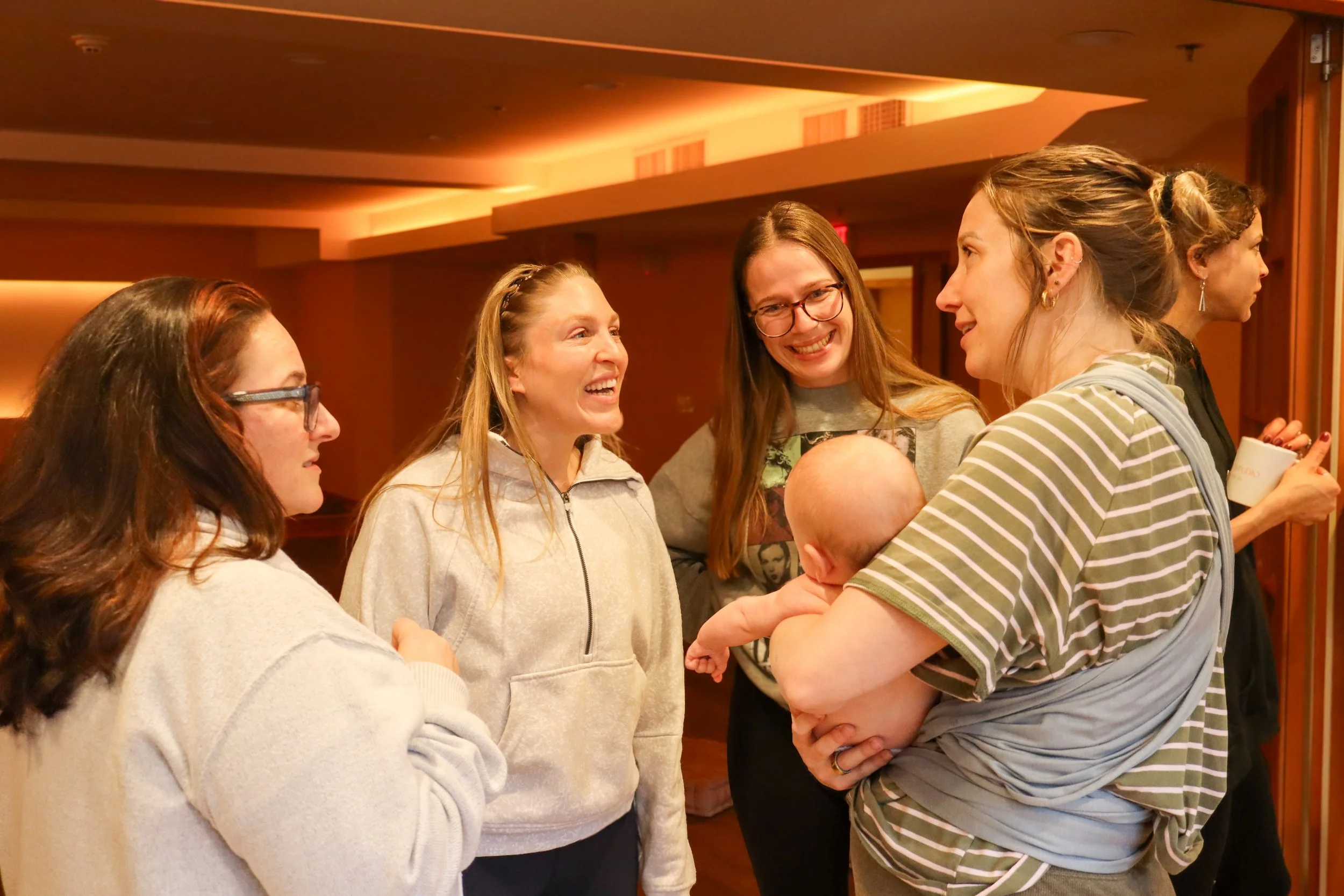A group of women standing and chatting indoors, engaged in conversation and smiling.