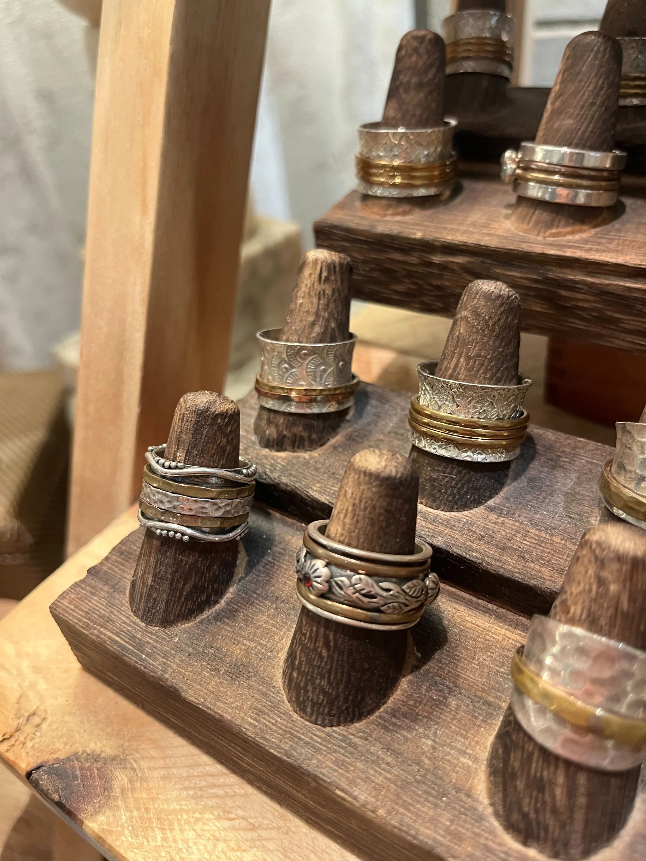 Close-up of a wooden jewelry display stand holding multiple rings, some with intricate silver designs and others gold bands, on small wooden pegs.