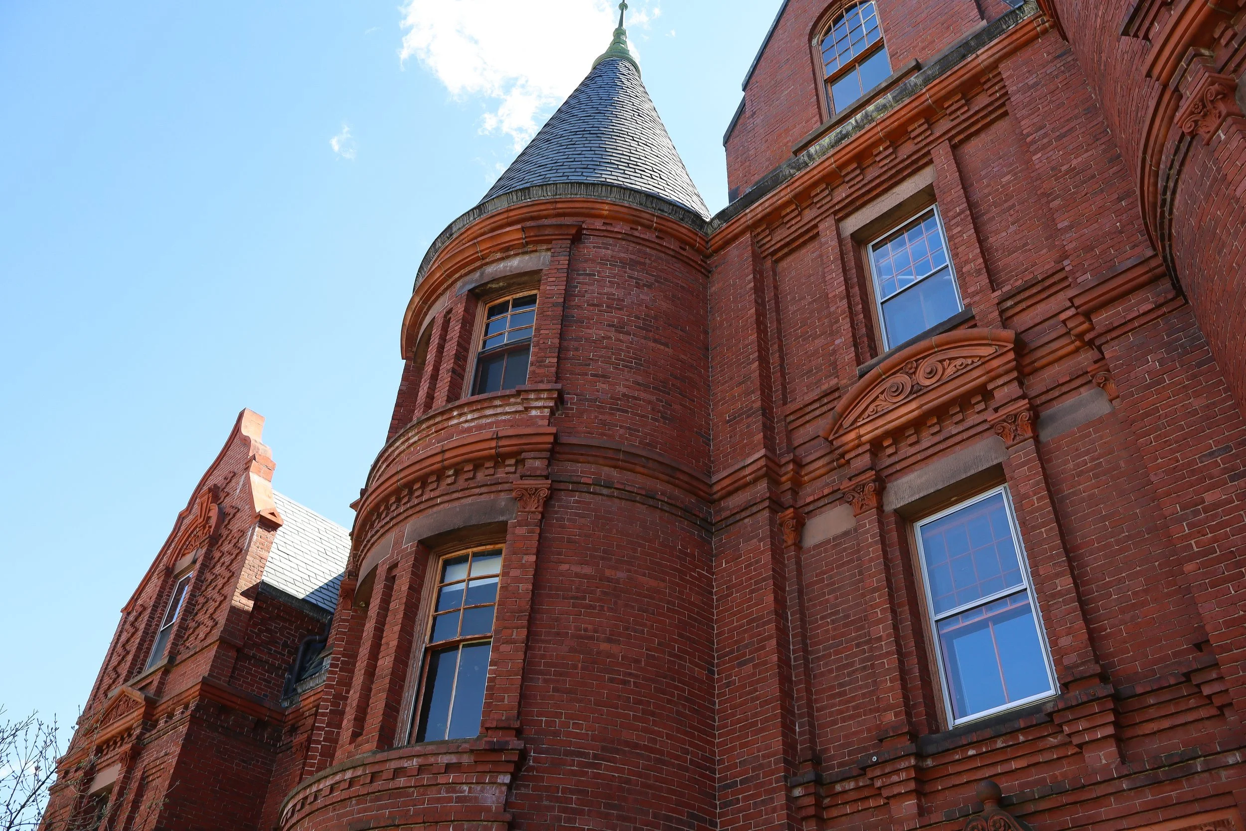 Close-up view of a red brick building with a turret and multiple windows, set against a partly cloudy sky.
