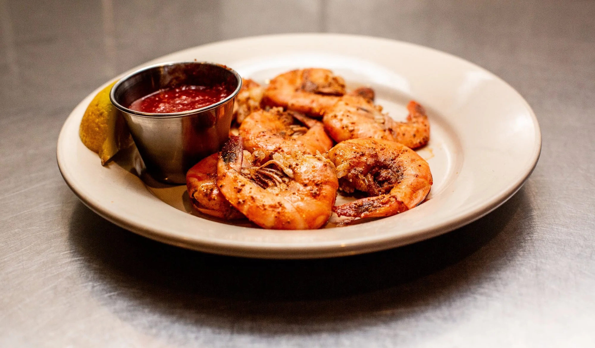 Plate of grilled shrimp with dipping sauce, lemon wedge, and lemon wedge on the side.