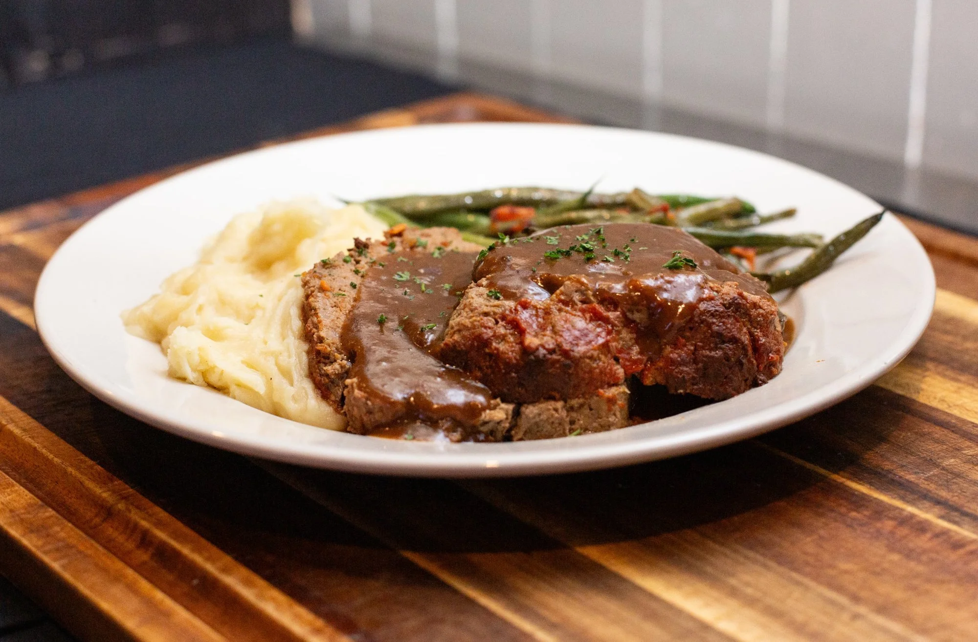 A plate of mashed potatoes, green beans, and Meat Loaf topped with gravy on a wooden table.