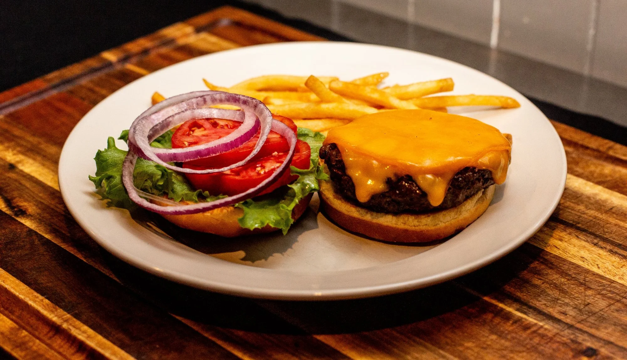 Cheeseburger on a white plate with French fries and a side salad of lettuce, tomato, and red onion, on a wooden table.